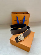 Dark belt with gold-toned monogram buckle on orange box, brown strap beneath.