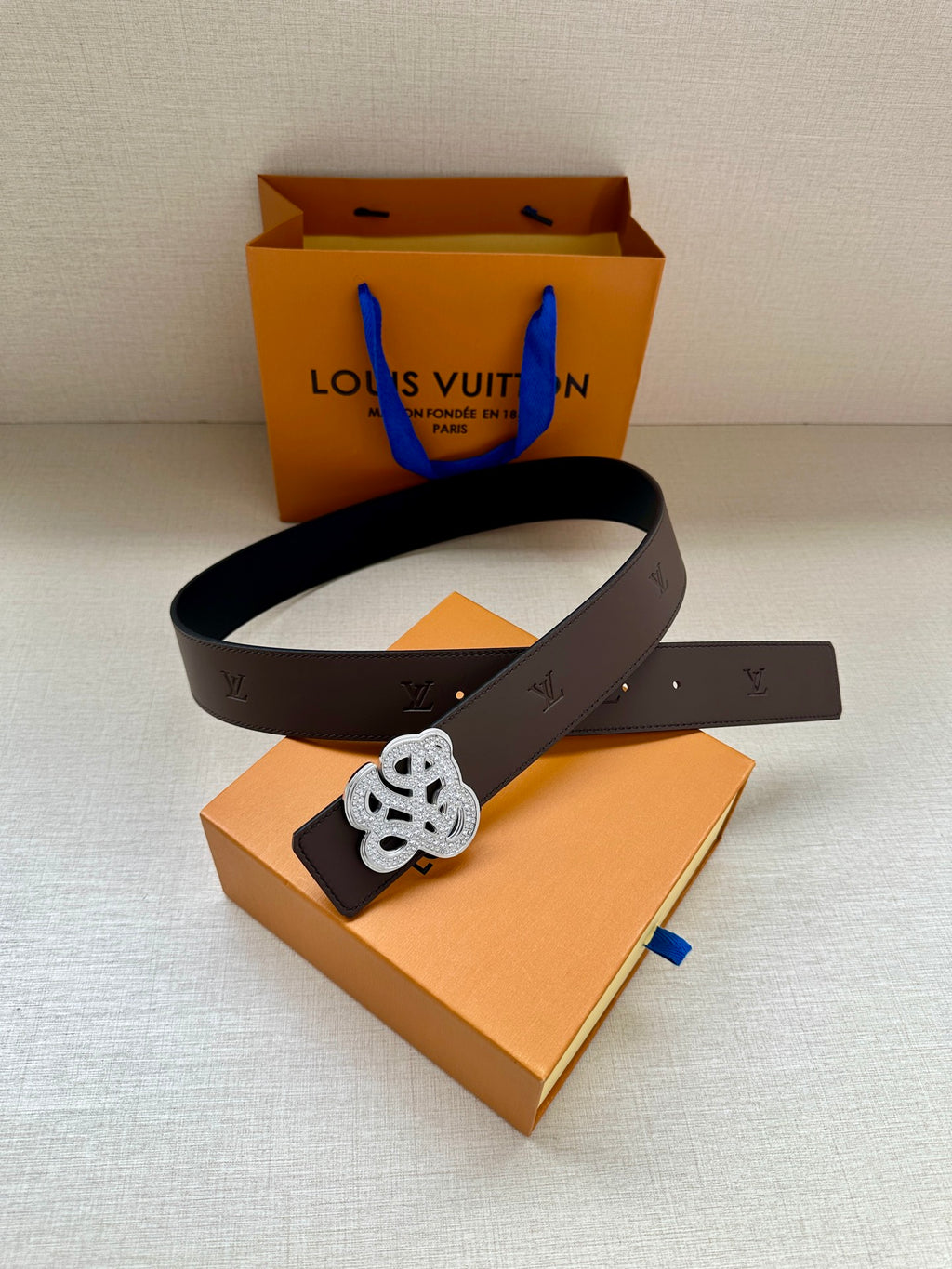 Dark belt with ornate silver monogram buckle laid on orange gift box and paper.