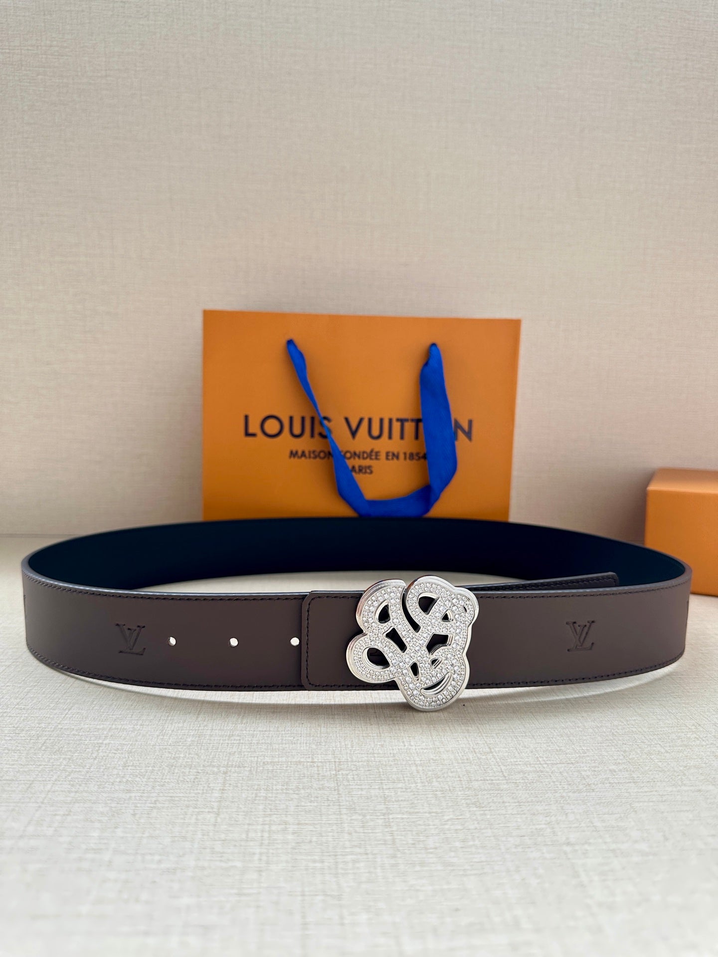 Brown leather belt with silver monogram buckle and dark lining panel on top.