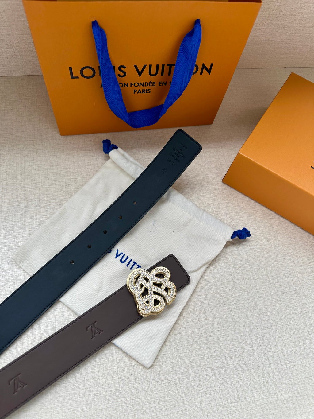 Dark belt strap with silver monogram buckle over white dust bag and blue ties.