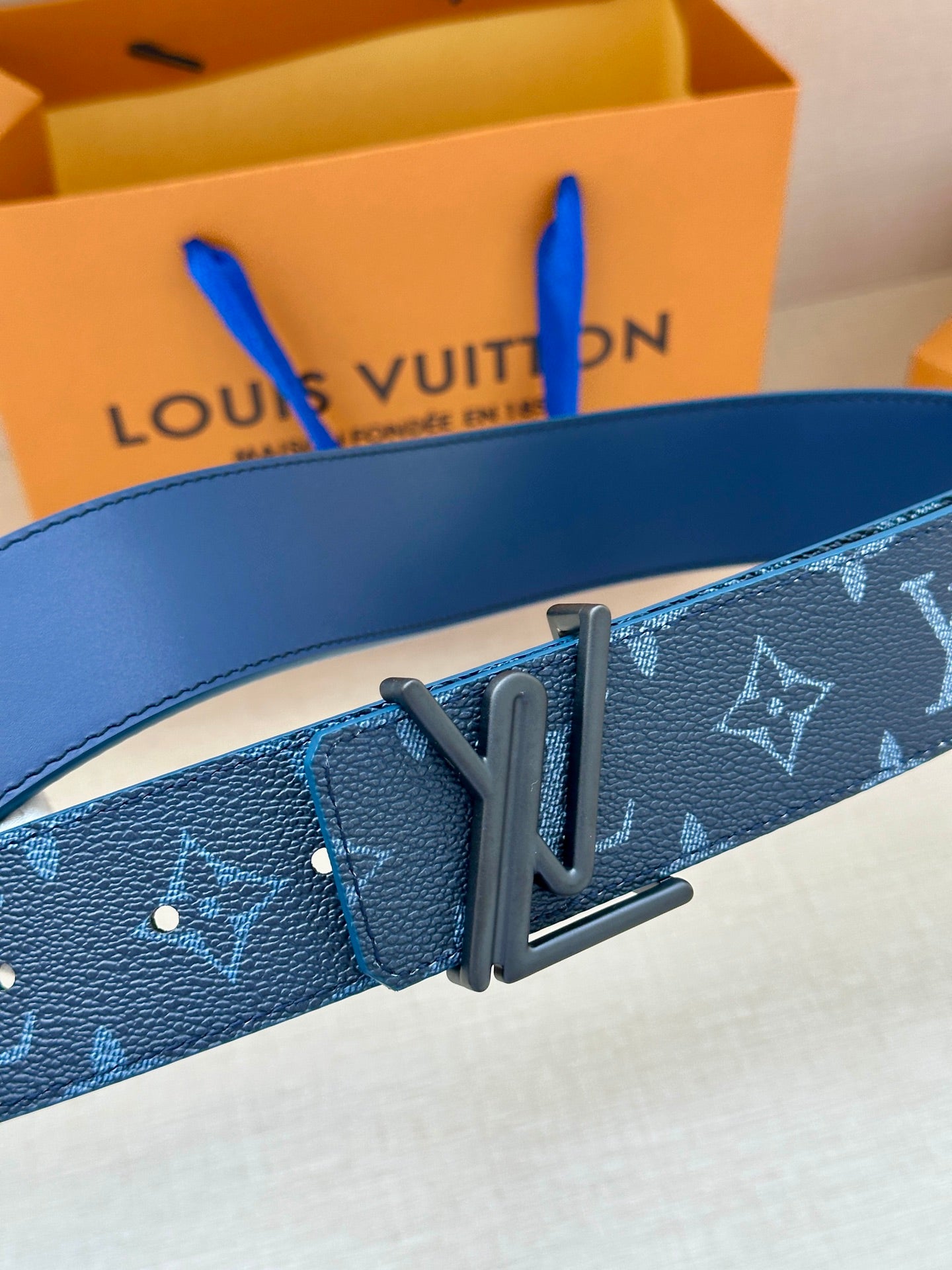 Blue monogram belt with dark buckle and metal logo plate
