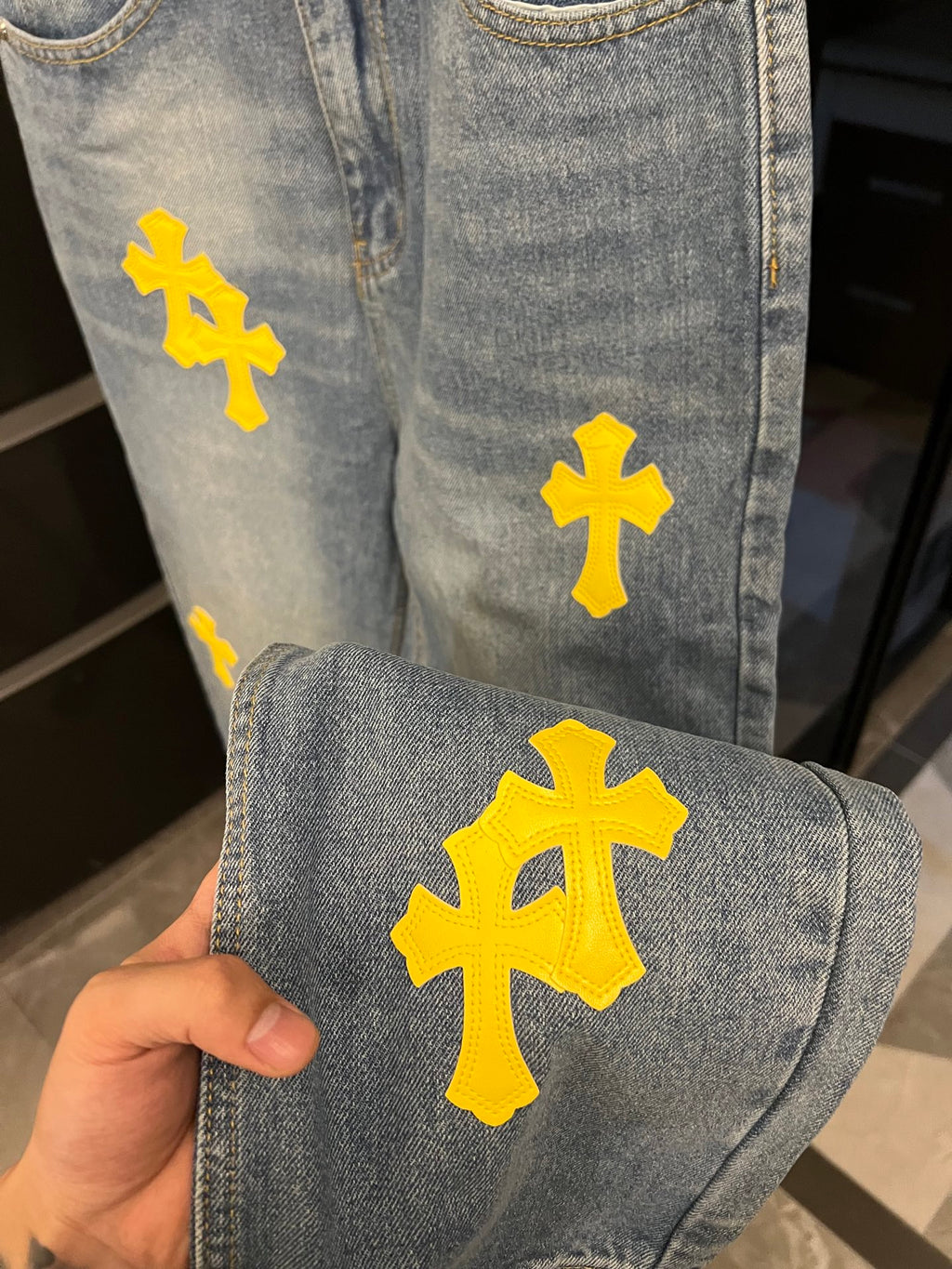 Light-wash denim jeans with large yellow cross patch on thigh