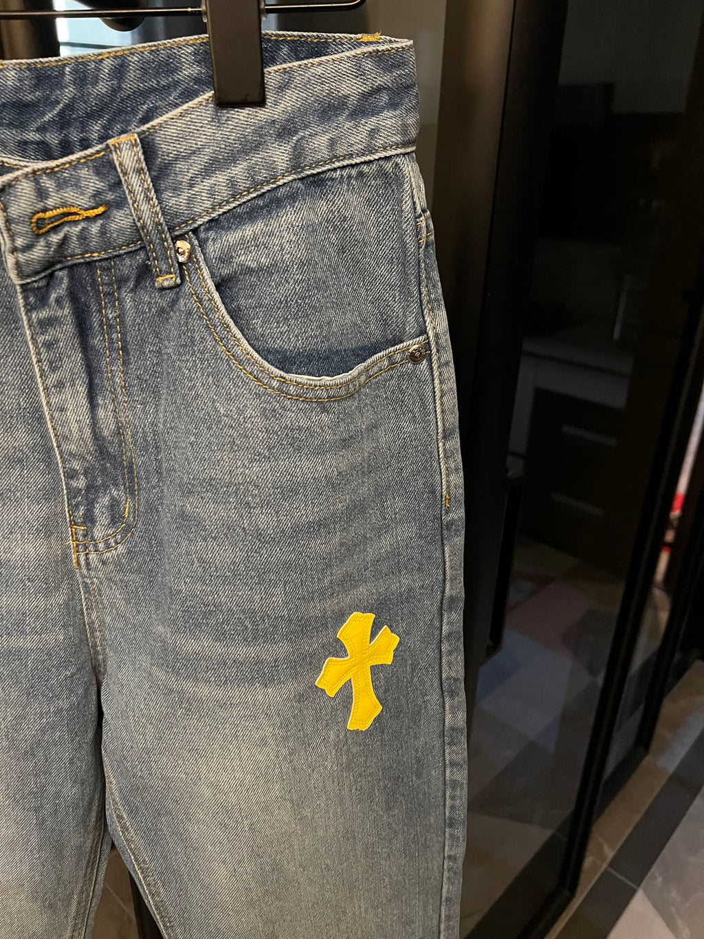 Light-wash denim jeans with yellow cross patch, side pocket area