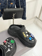 Balenciaga black slip-on clogs with studded charms, one shoe angled
