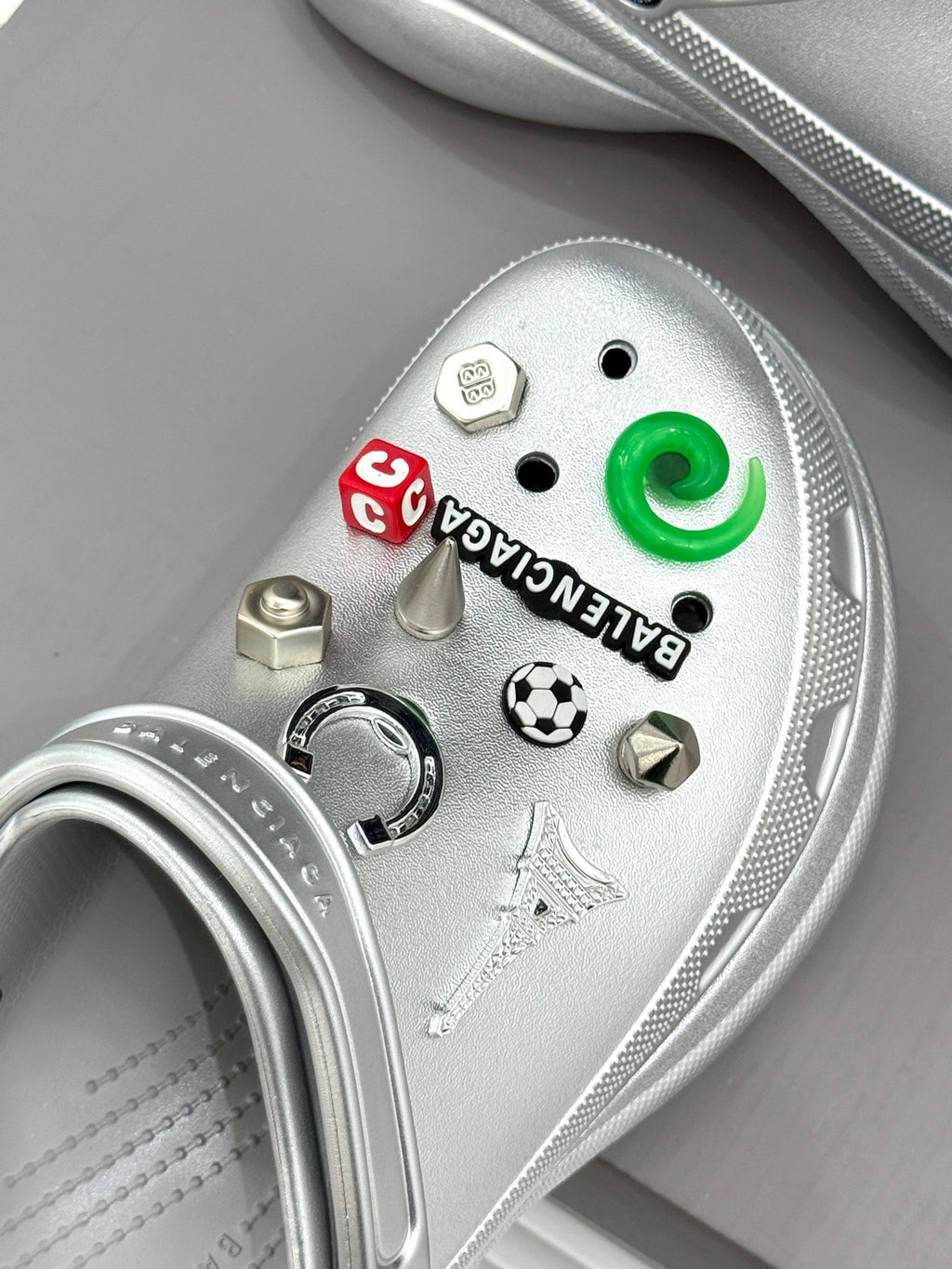 Close-up of silver clog top with green button and charm and sticker details