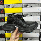 Black lace-up sneakers held in hand, side profile with chunky midsole and logo