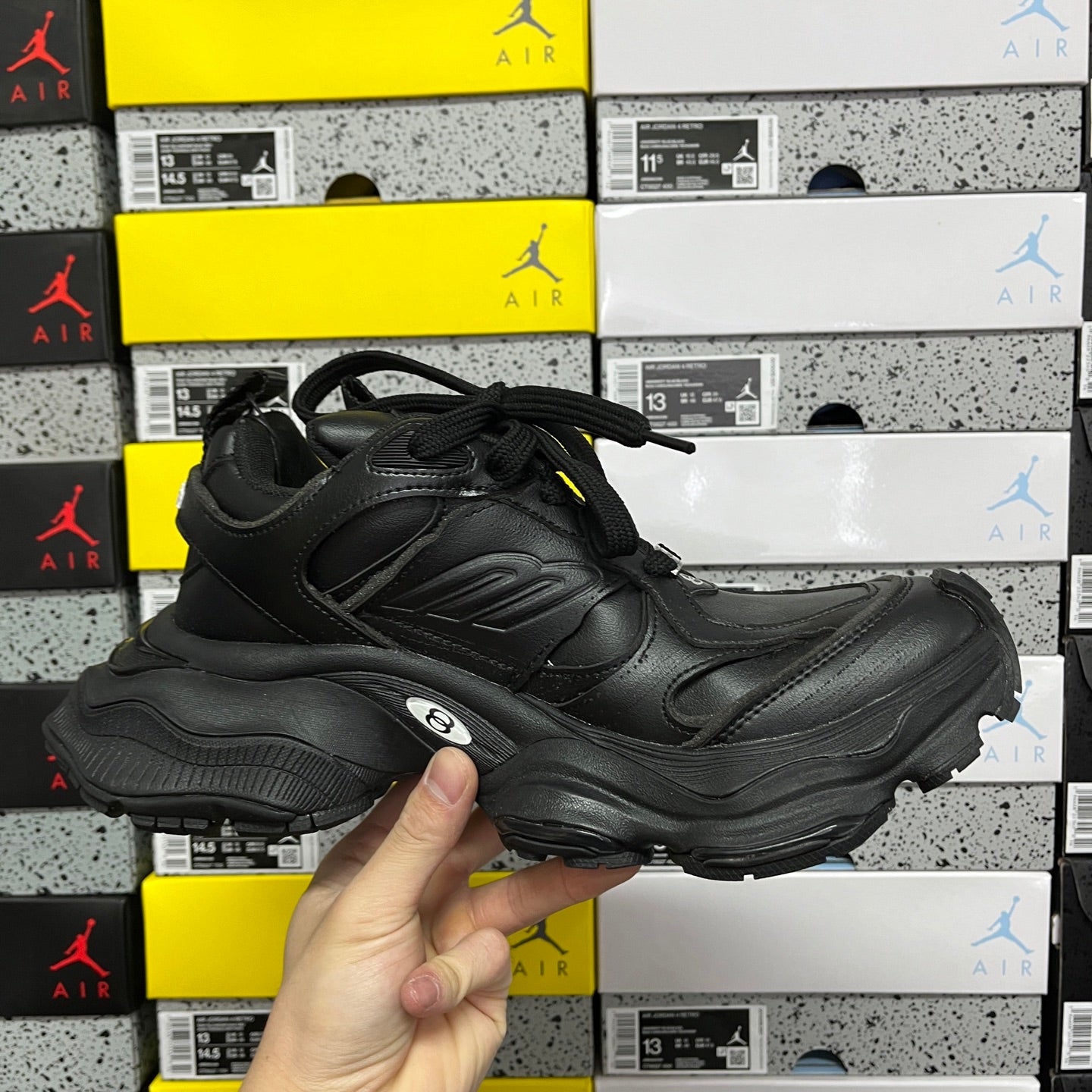 Black lace-up sneakers held in hand, side profile with chunky midsole and logo