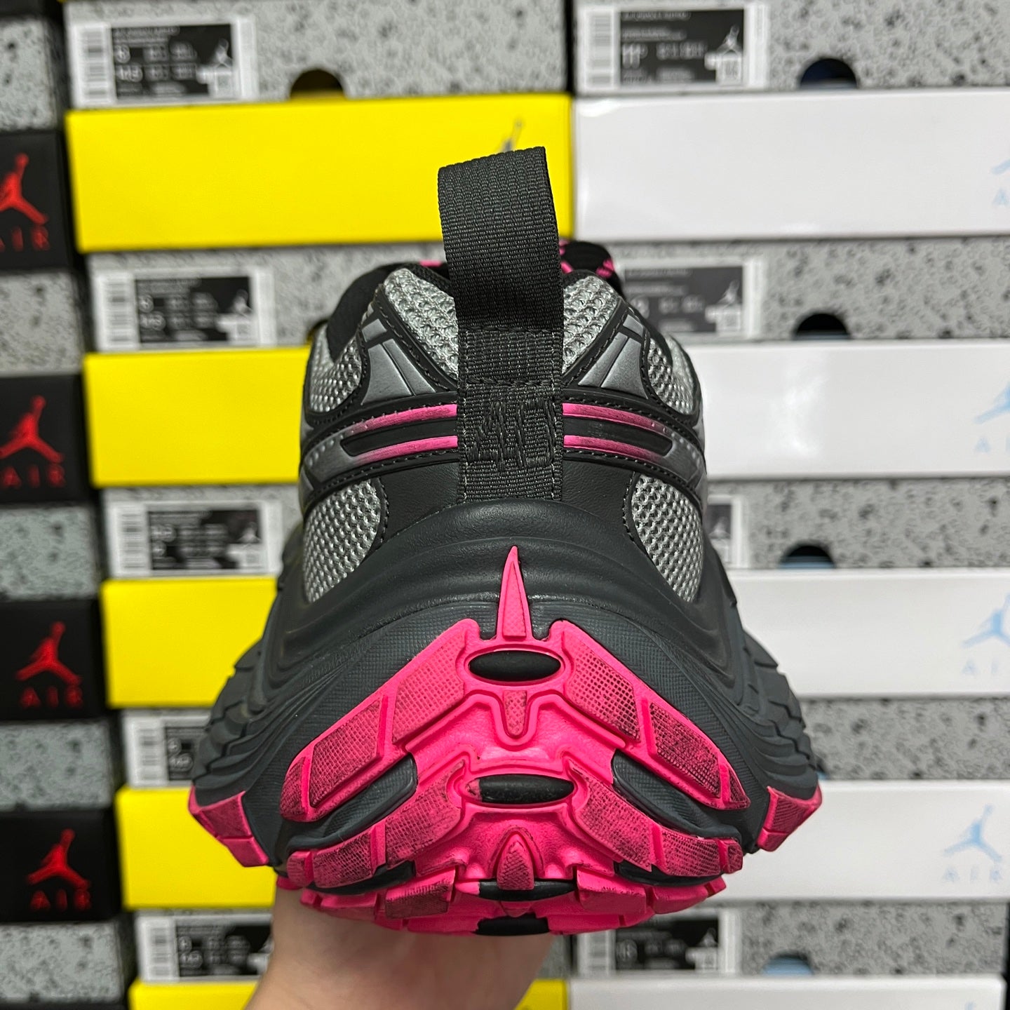 Heel view of black running shoe with pink stripe accents and thick tread sole.