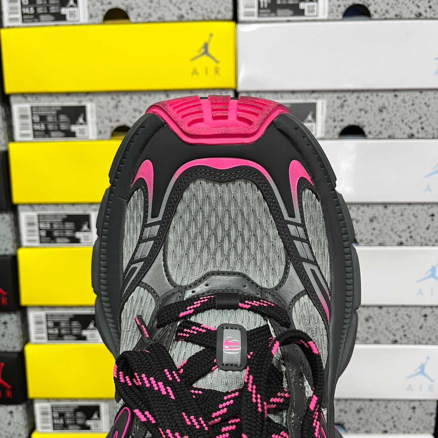 Front view of black running shoe with gray mesh, pink-patterned laces, and tongue pull.