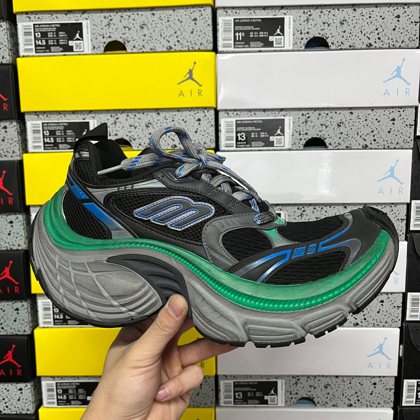 Chunky black sneaker with gray sole, blue accents, green trim, and lace-up upper