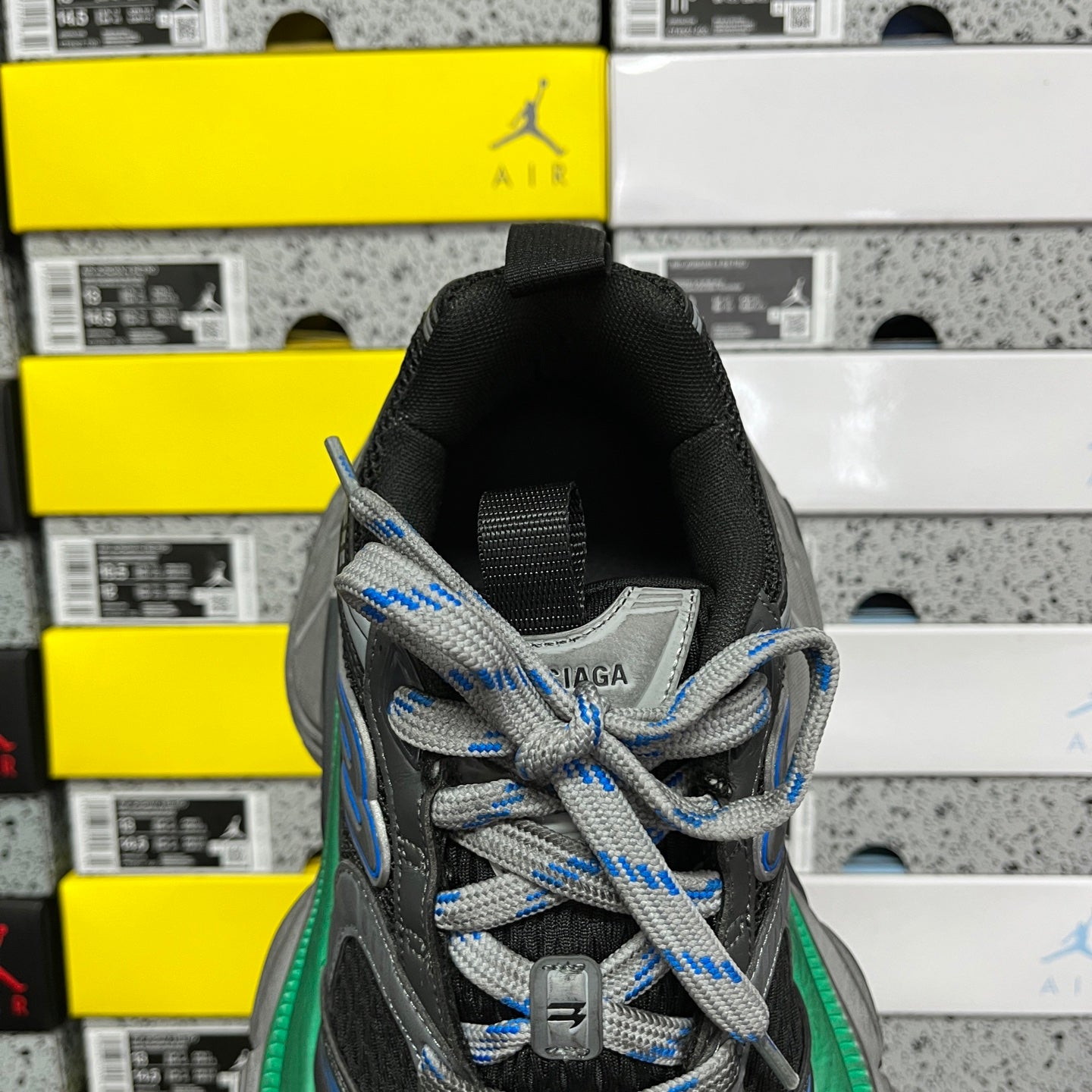 Front view of black sneaker with blue-and-gray laces and green-trimmed midsole