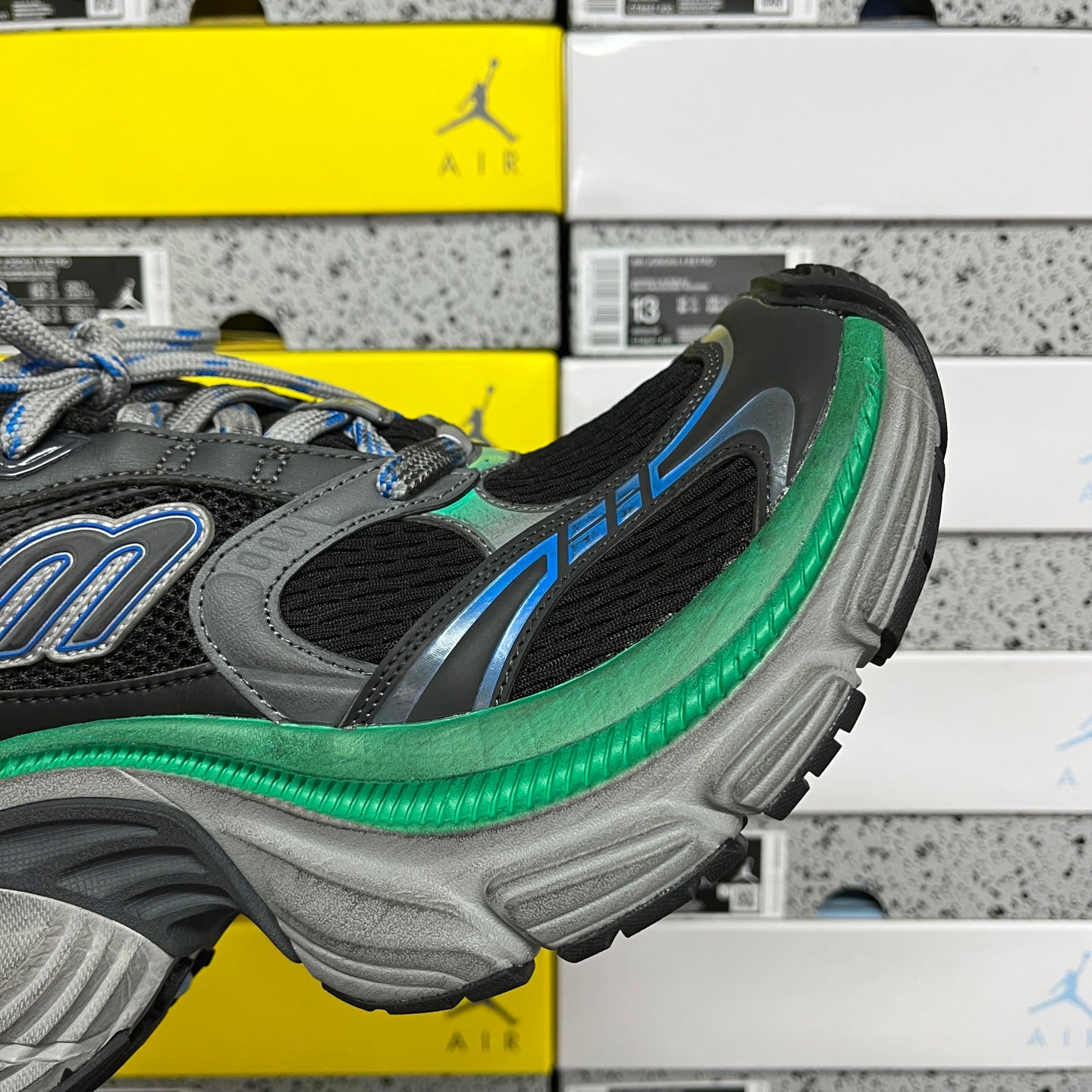 Side view of black sneaker with blue accents, green midsole trim, and textured gray outsole