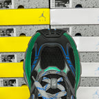 Top view of black sneaker with blue side stripes, green collar trim, and lace closure