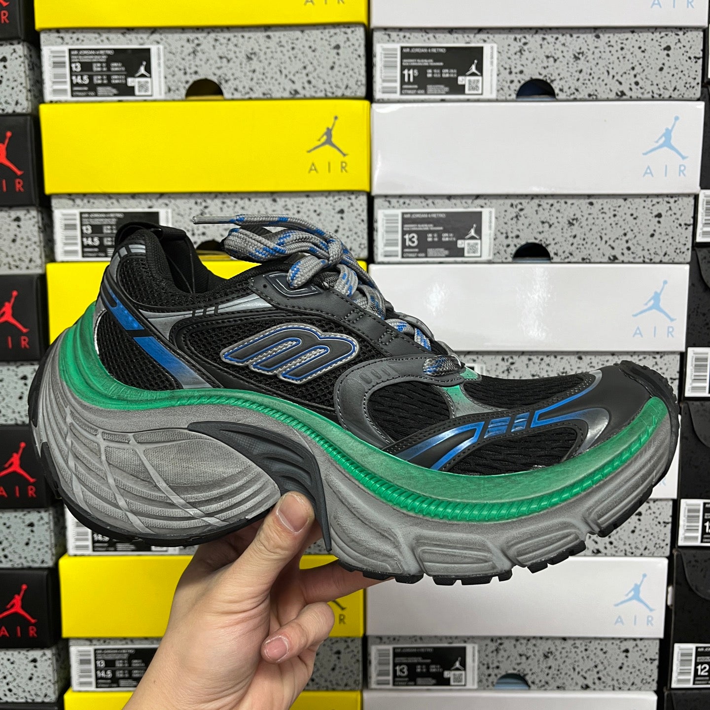 Lace-up black sneaker with blue details, green midsole trim, and gray molded outsole