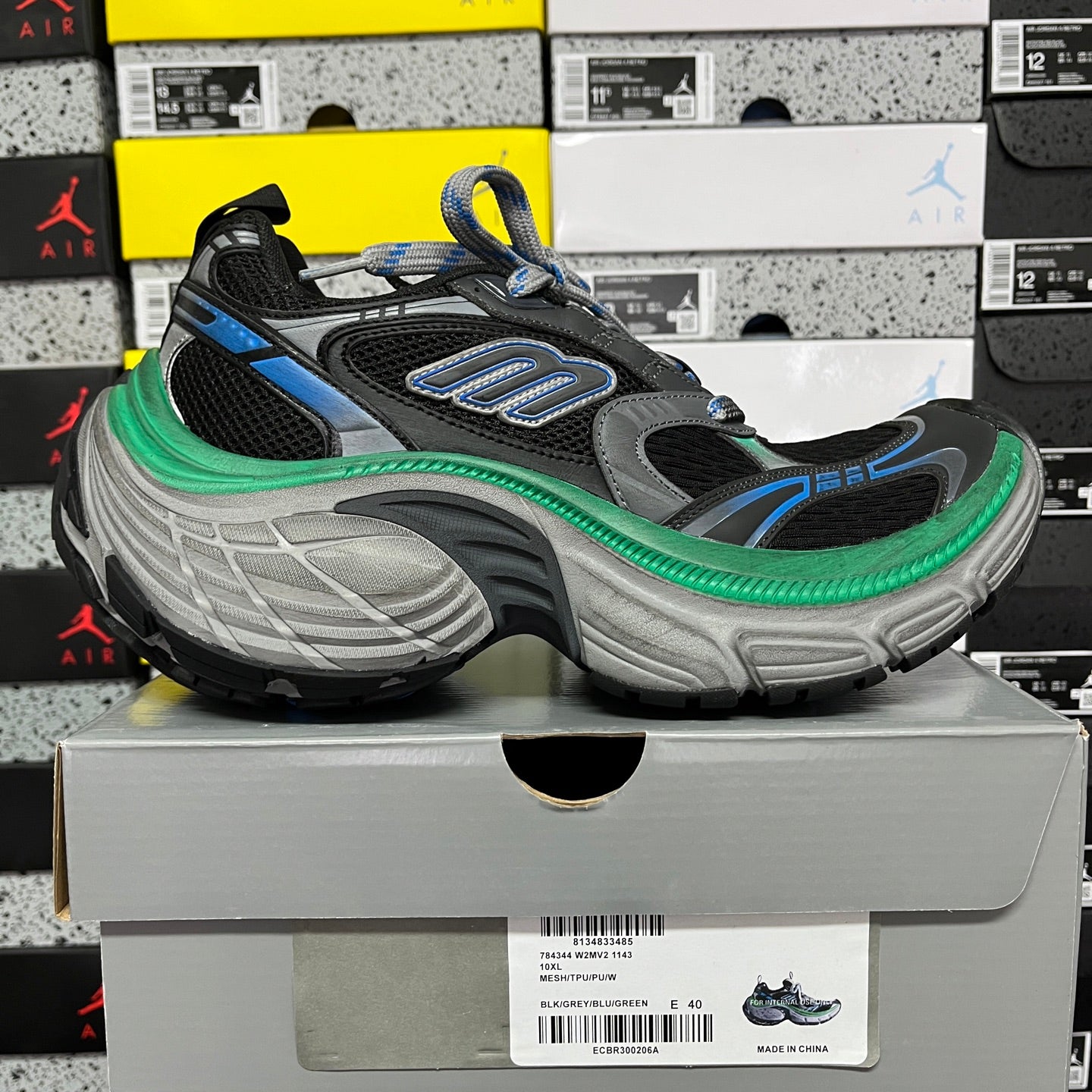 Black lace-up sneaker on gray sole with blue logo details and green edge piping