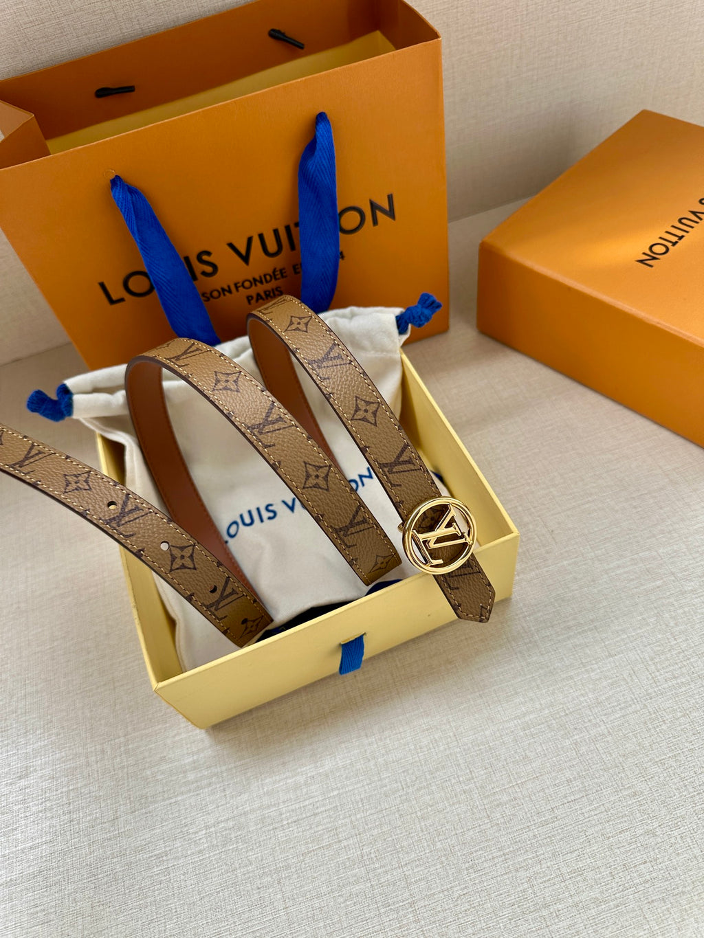 Louis Vuitton monogram belt with gold buckle laid across a box