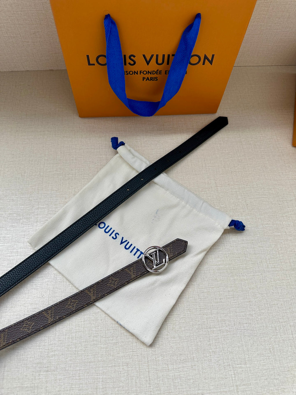 Dark monogram belt with round silver-tone LV buckle on white dust bag