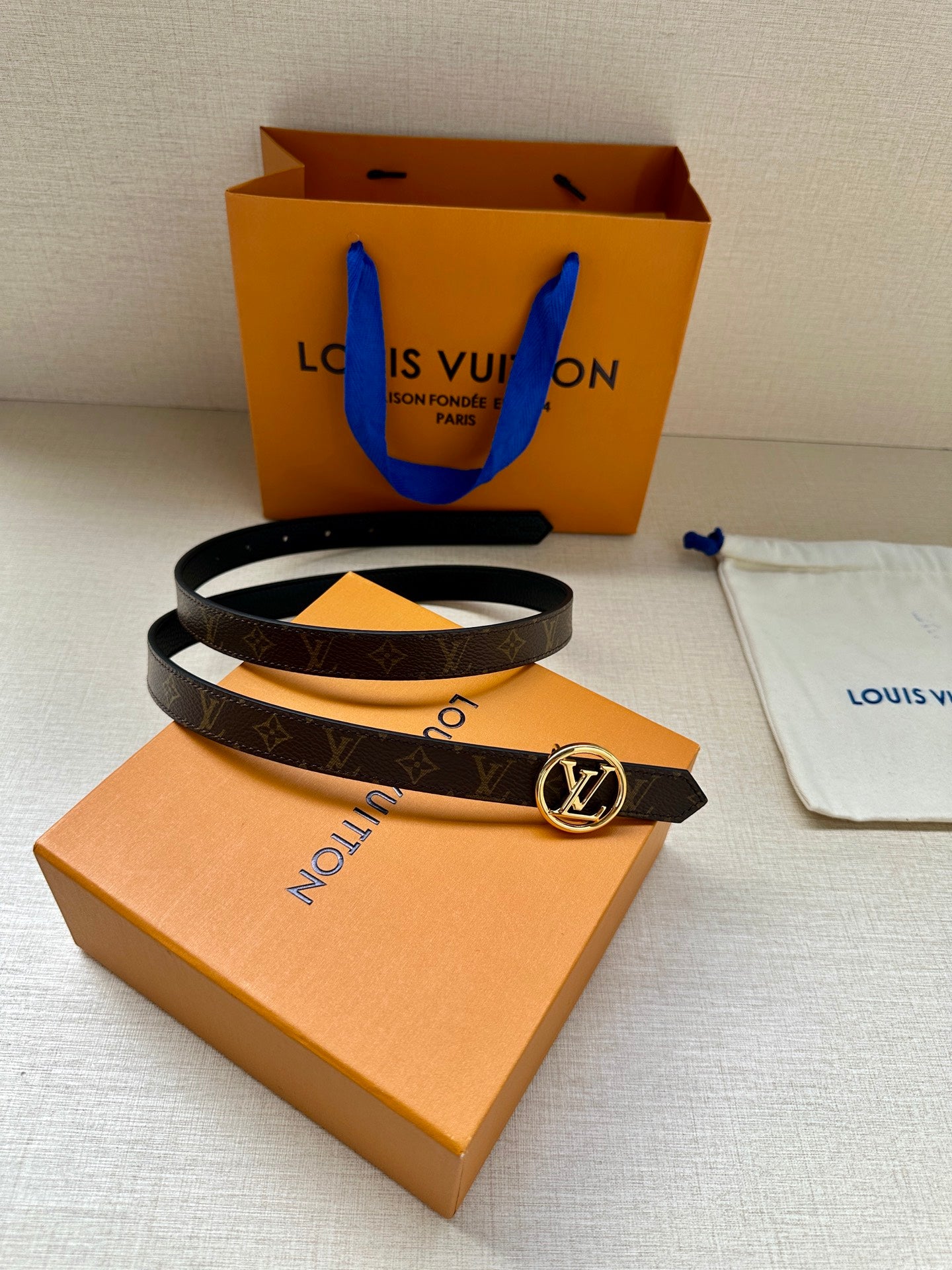 Dark monogram belt with round silver-tone LV buckle on orange box