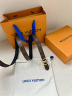 Dark monogram belt with round silver-tone LV buckle beside Louis Vuitton boxes