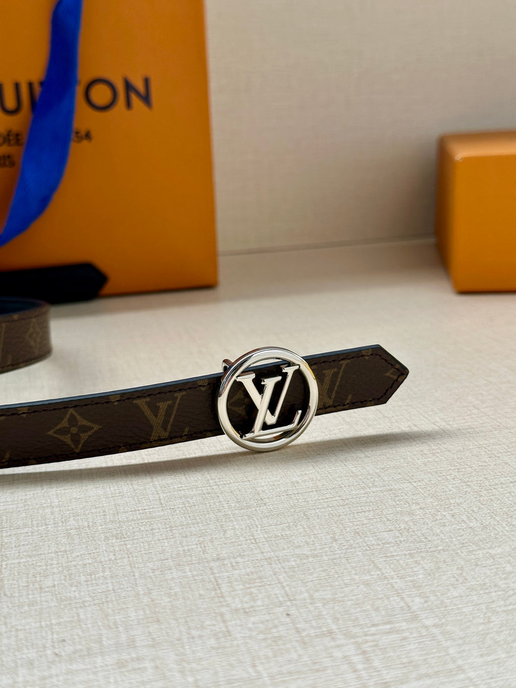 Dark monogram belt laying flat with round silver-tone LV logo buckle
