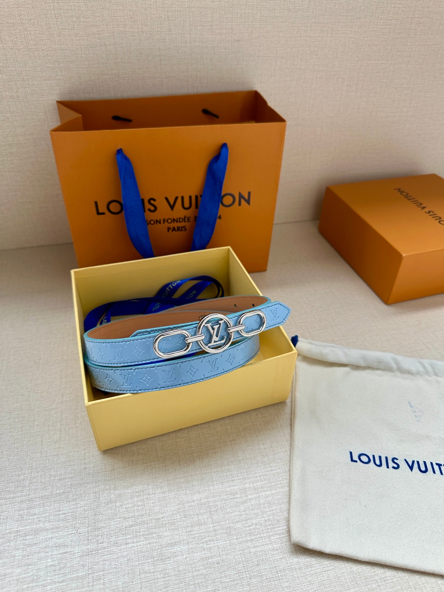 Light blue Louis Vuitton belt with gold LV buckle in a small box and dust bag.
