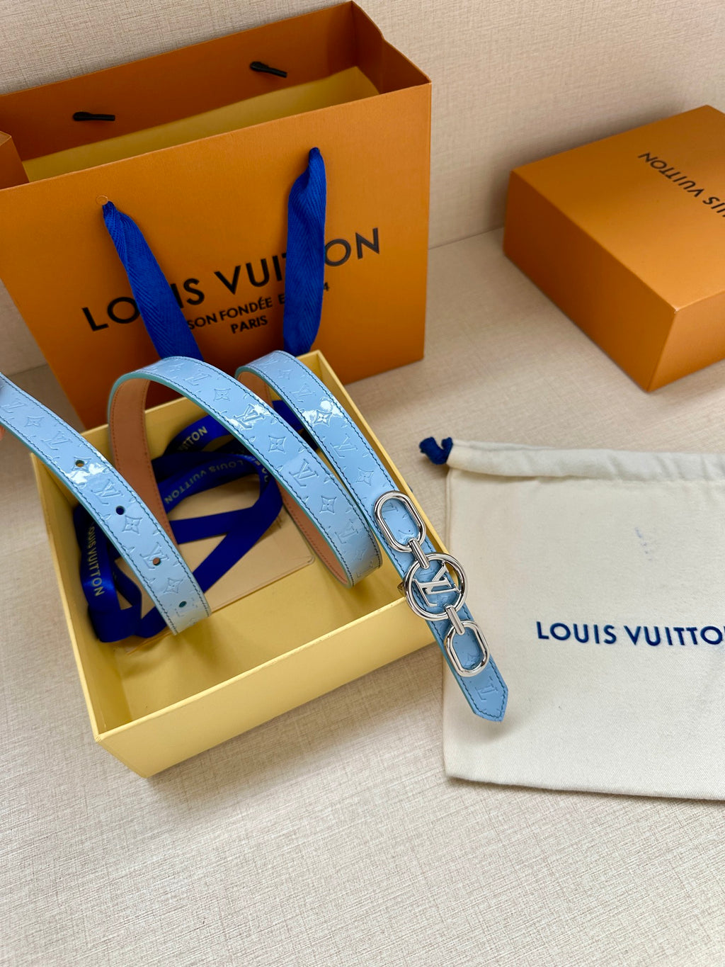 Light blue leather belt with gold LV buckle, shown with matching strap pieces.
