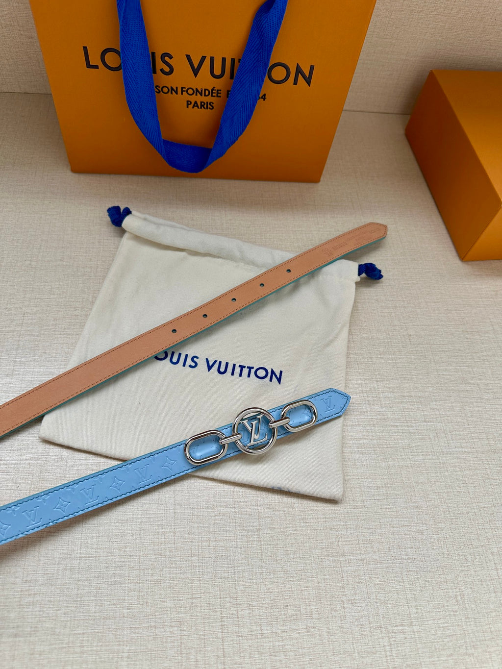 Tan leather belt strap with rivet holes, beside light blue gold LV buckle belt.