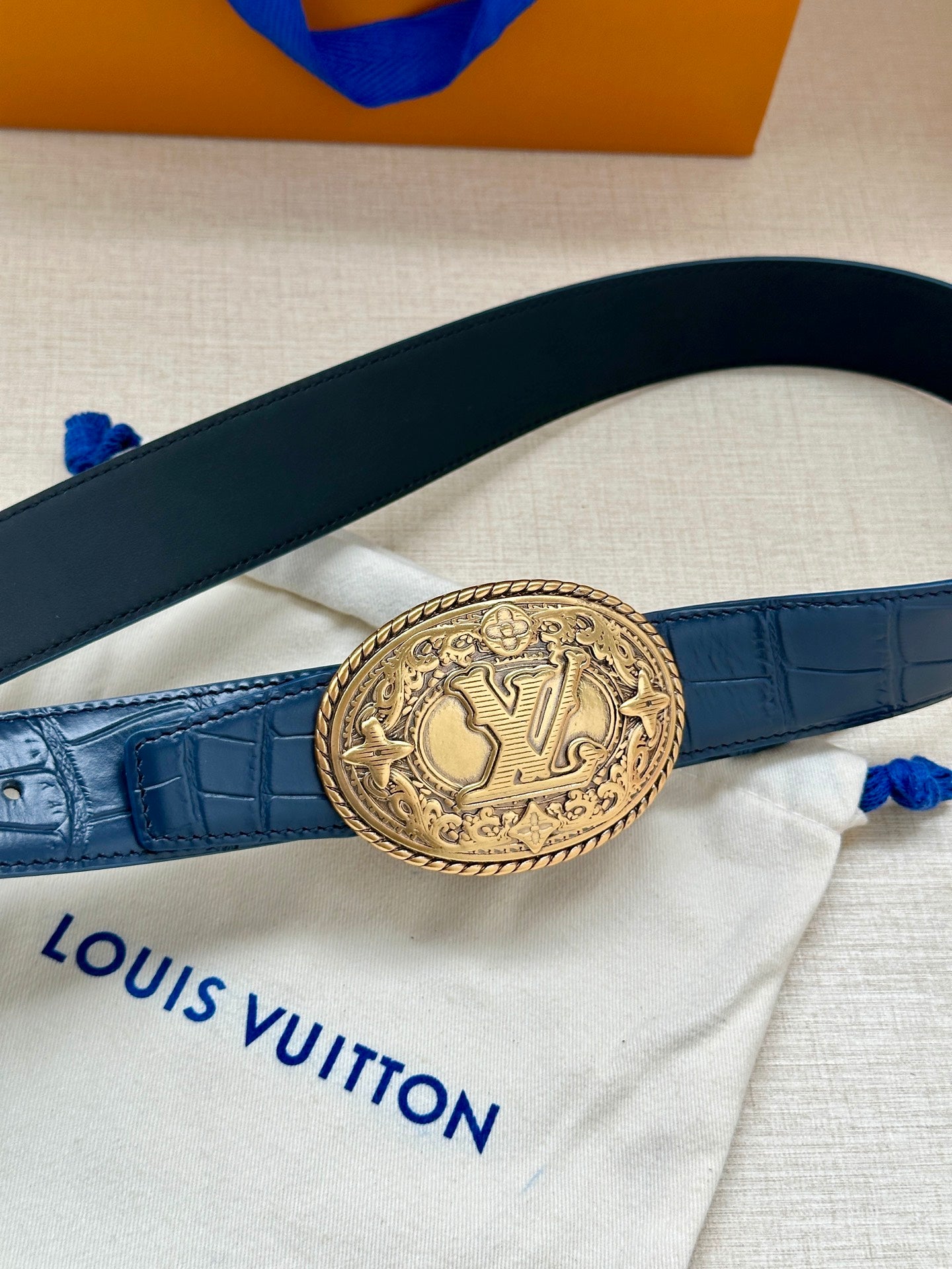 Louis Vuitton dark blue leather belt with gold oval logo buckle across strap