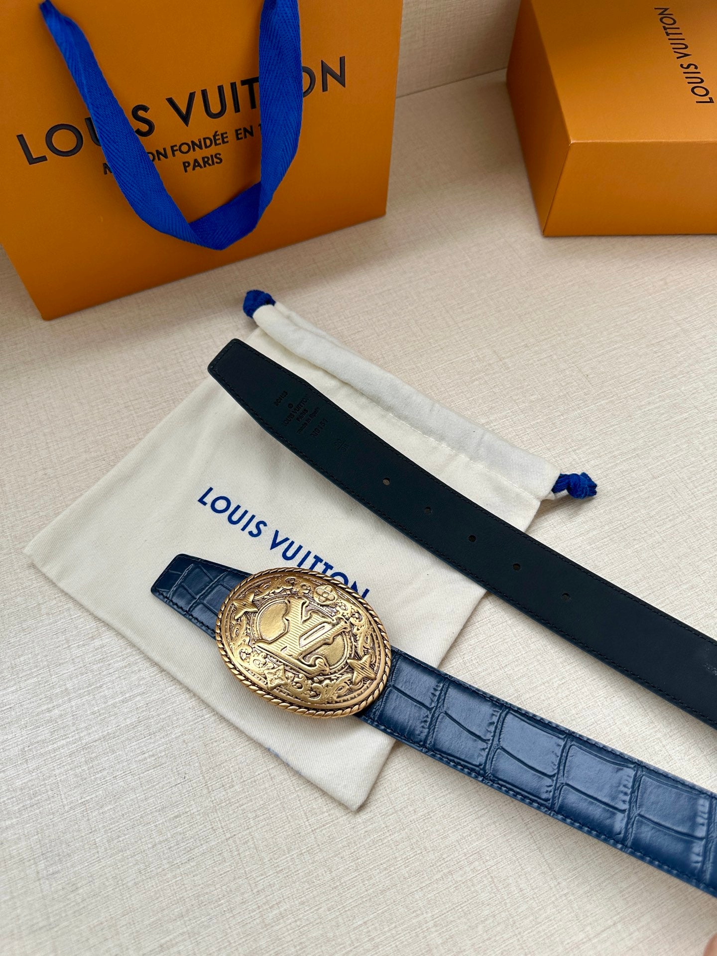 Louis Vuitton dark blue leather belt with gold oval logo buckle, flat lay
