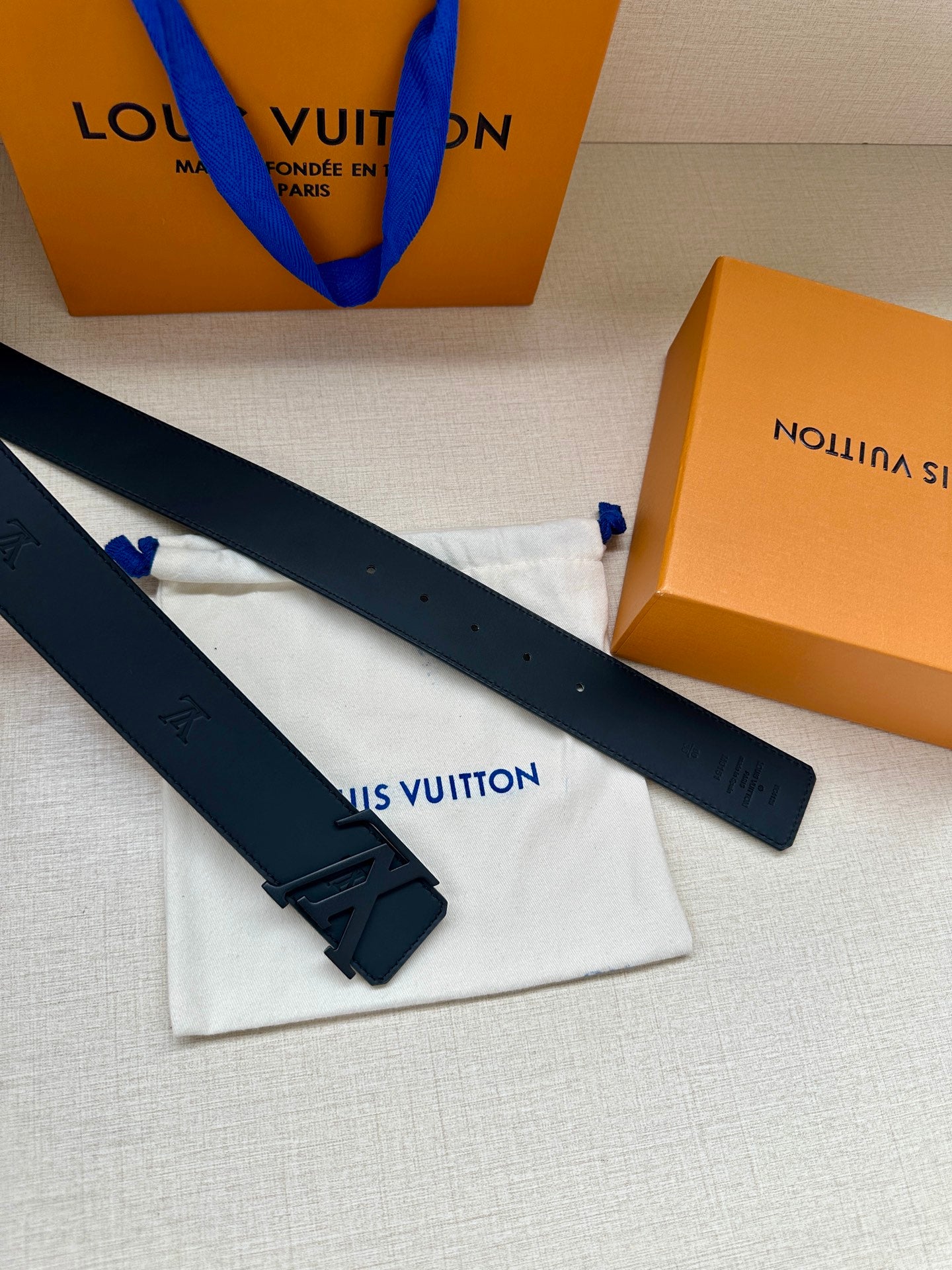 Louis Vuitton belt straps with dark buckle and embossed logo, laid across dust bag