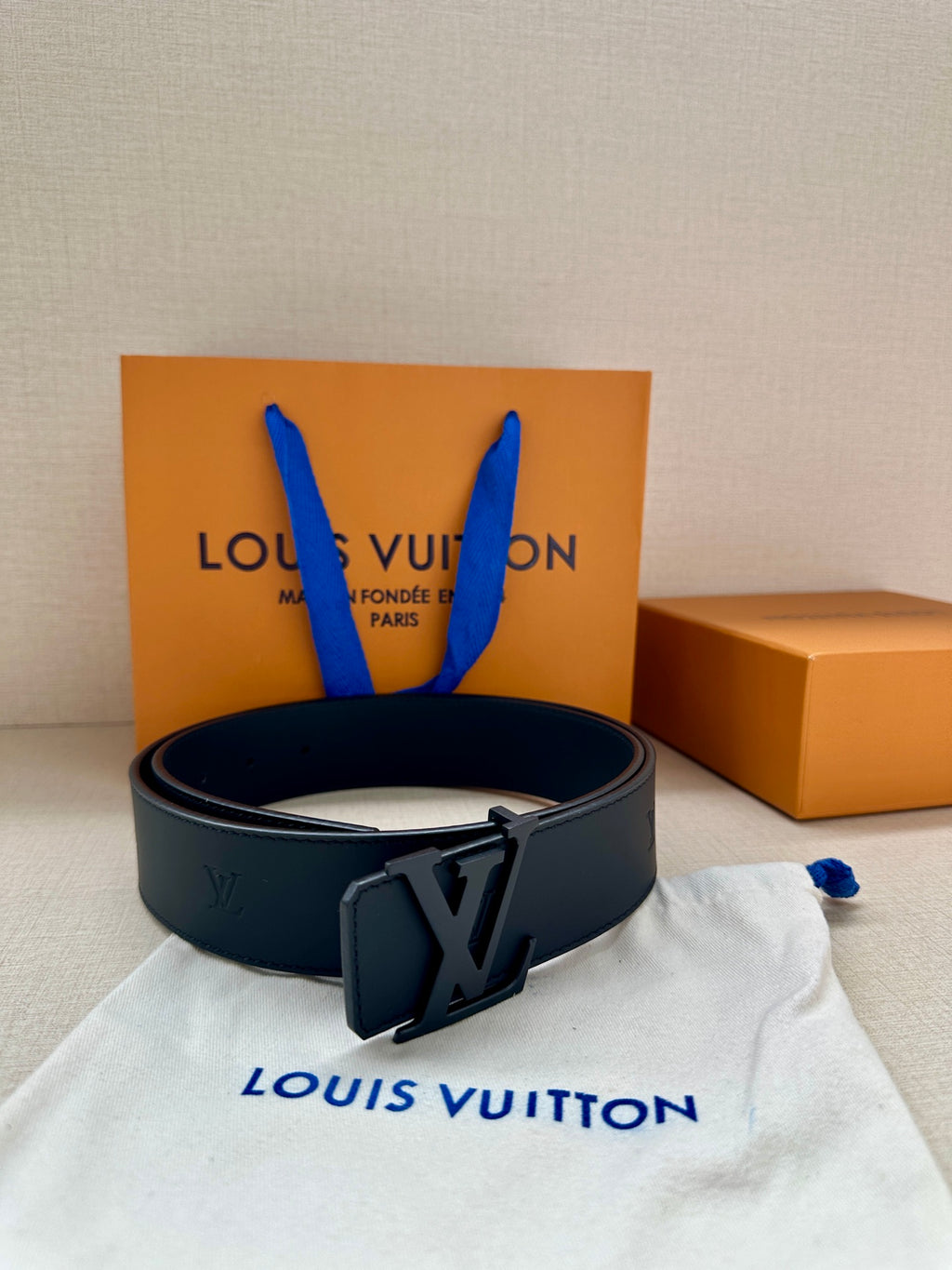 Louis Vuitton leather belt with dark buckle, arranged on white dust bag