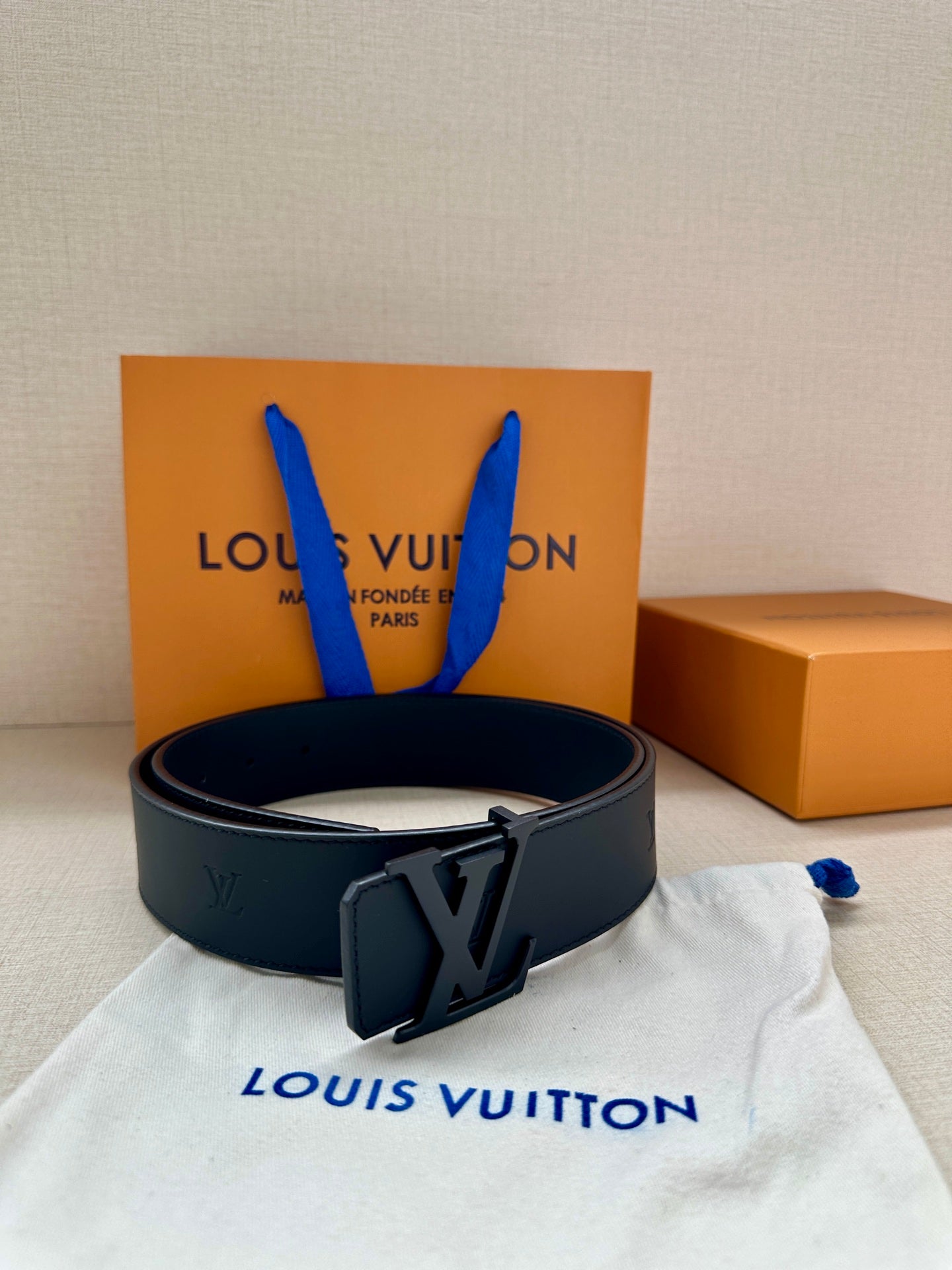 Louis Vuitton leather belt with dark buckle, arranged on white dust bag