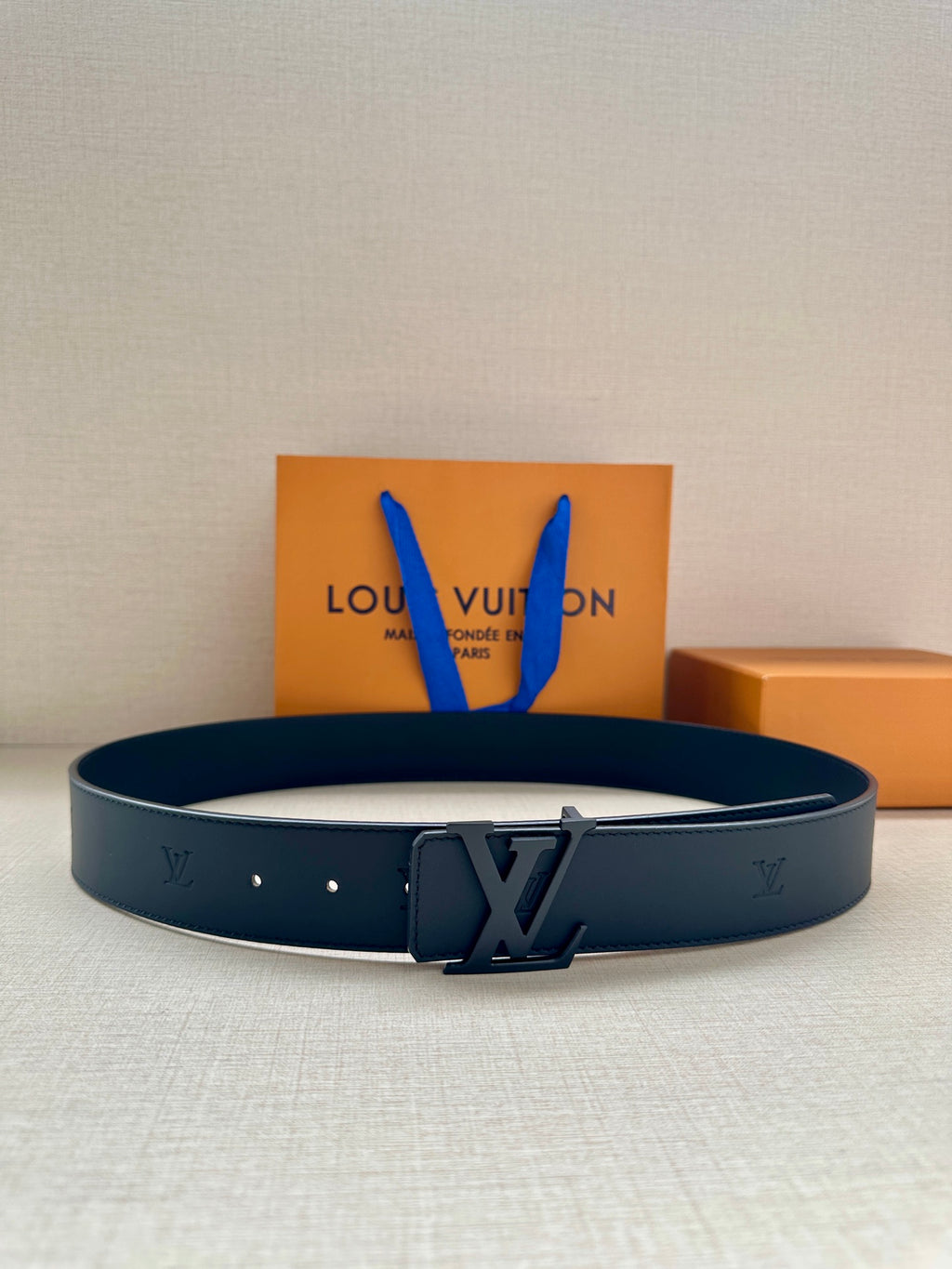 Louis Vuitton leather belt with dark buckle and stitched holes, coiled view