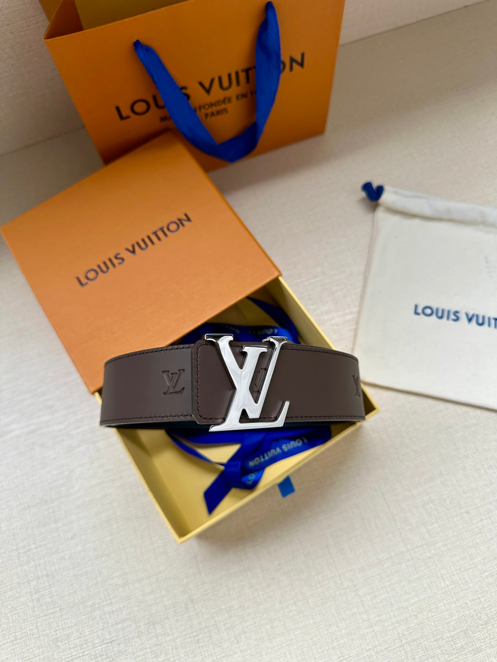 Louis Vuitton belt with dark strap and gold LV buckle, folded on a gift box