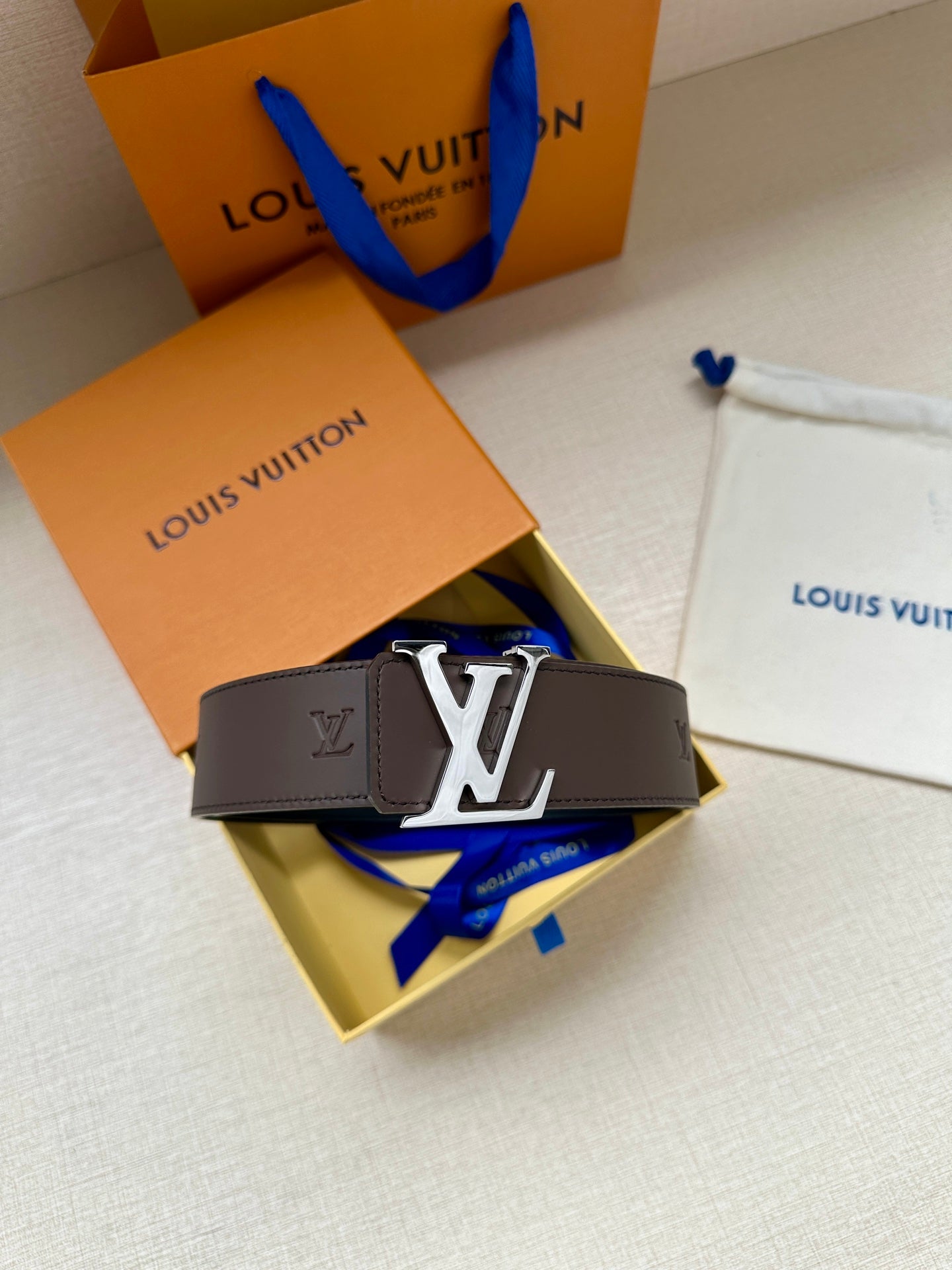 Louis Vuitton belt with dark strap and gold LV buckle, folded on a gift box