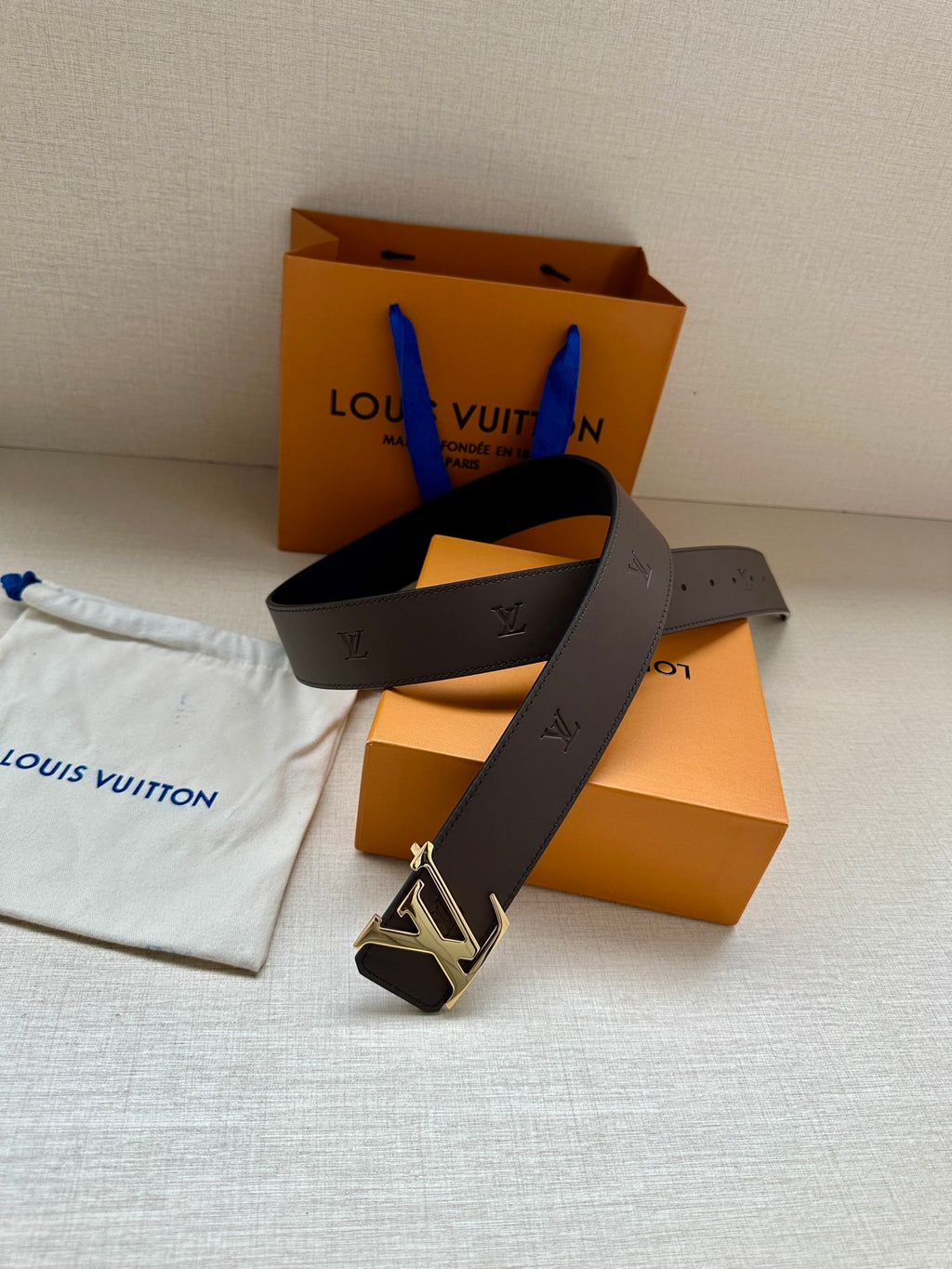 Louis Vuitton belt with dark leather strap and gold LV buckle, angled view