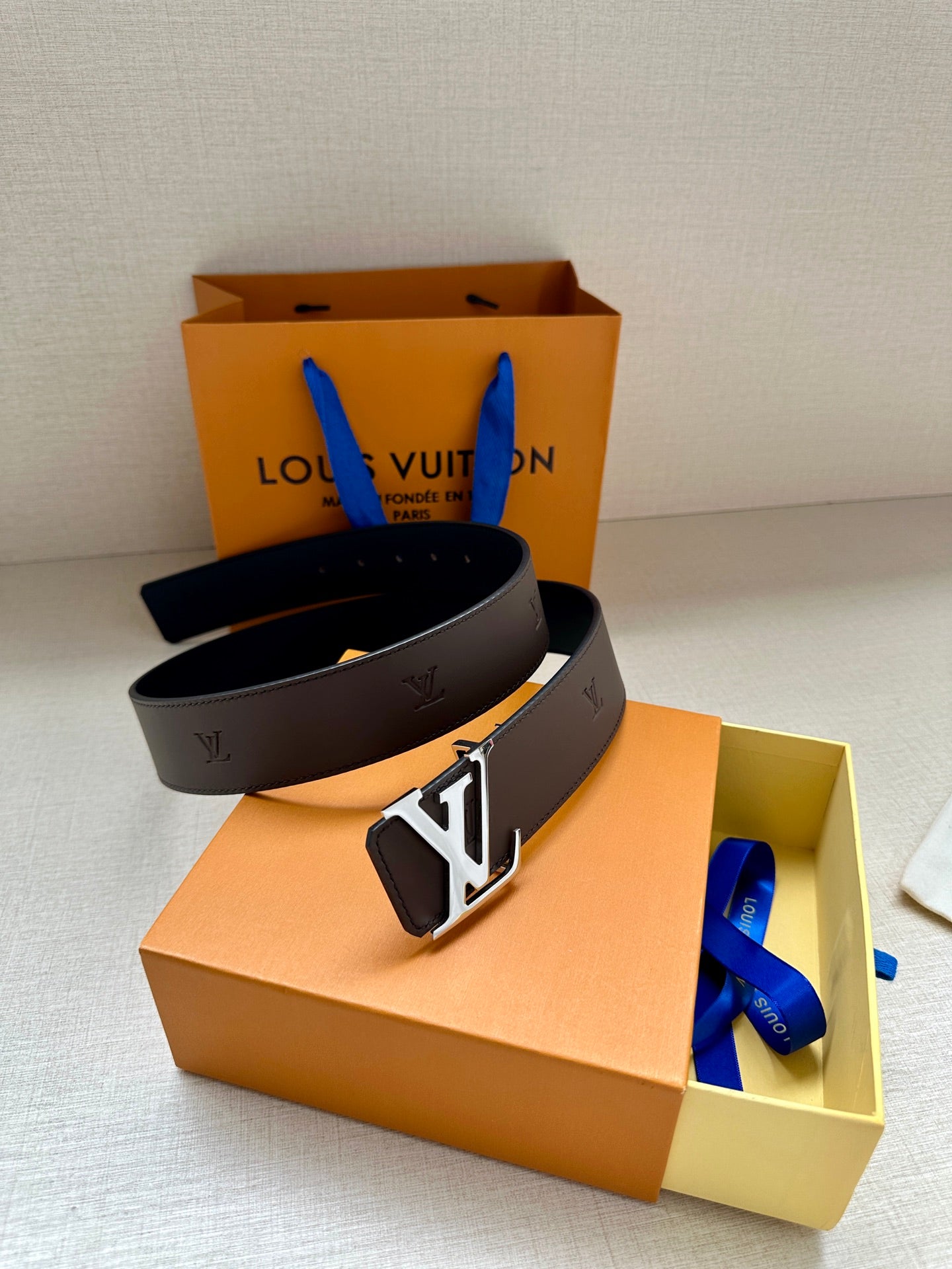 Louis Vuitton belt with dark strap and gold LV buckle, resting on a box
