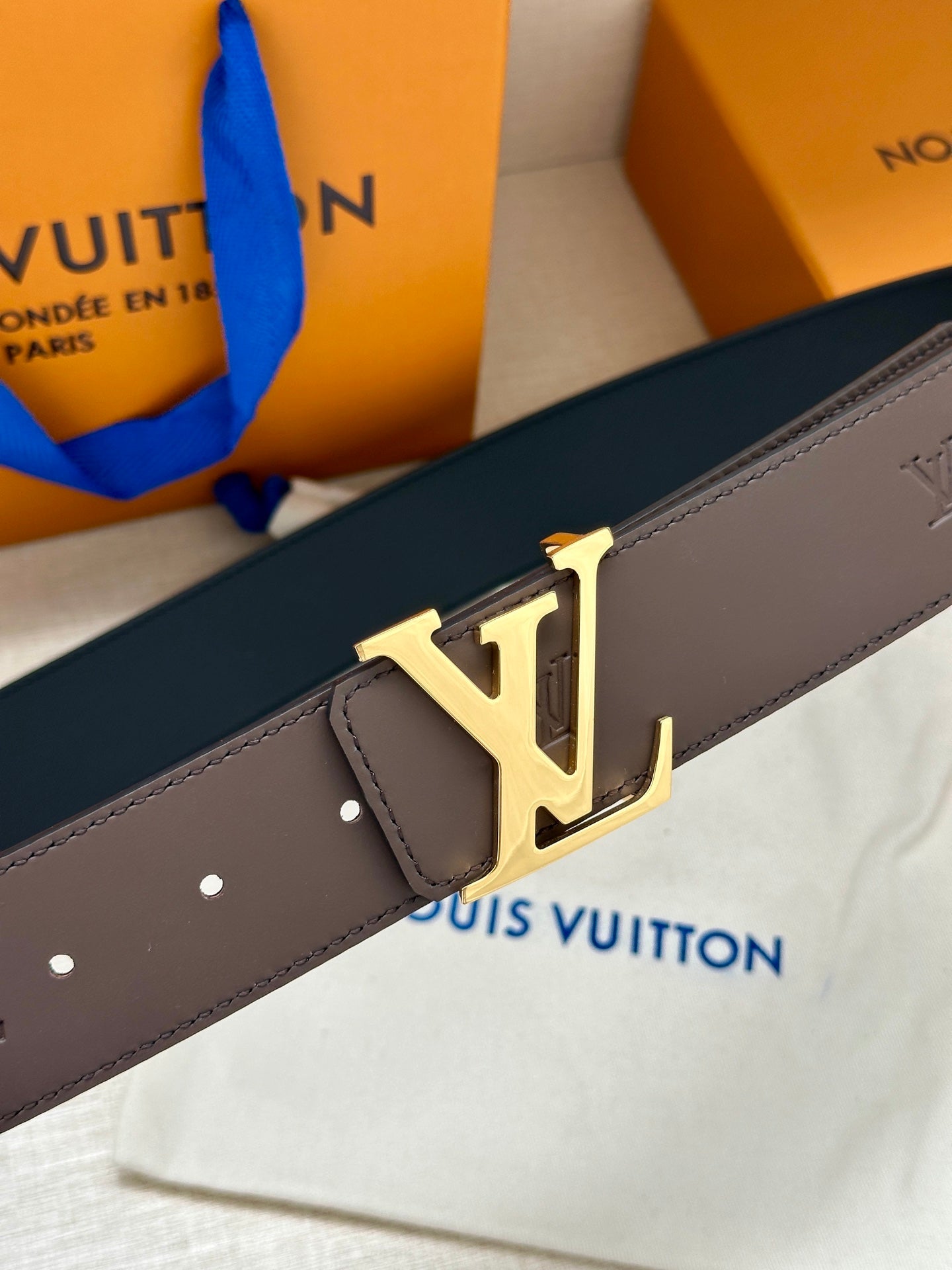 Louis Vuitton belt close-up: dark strap with gold LV buckle and small holes