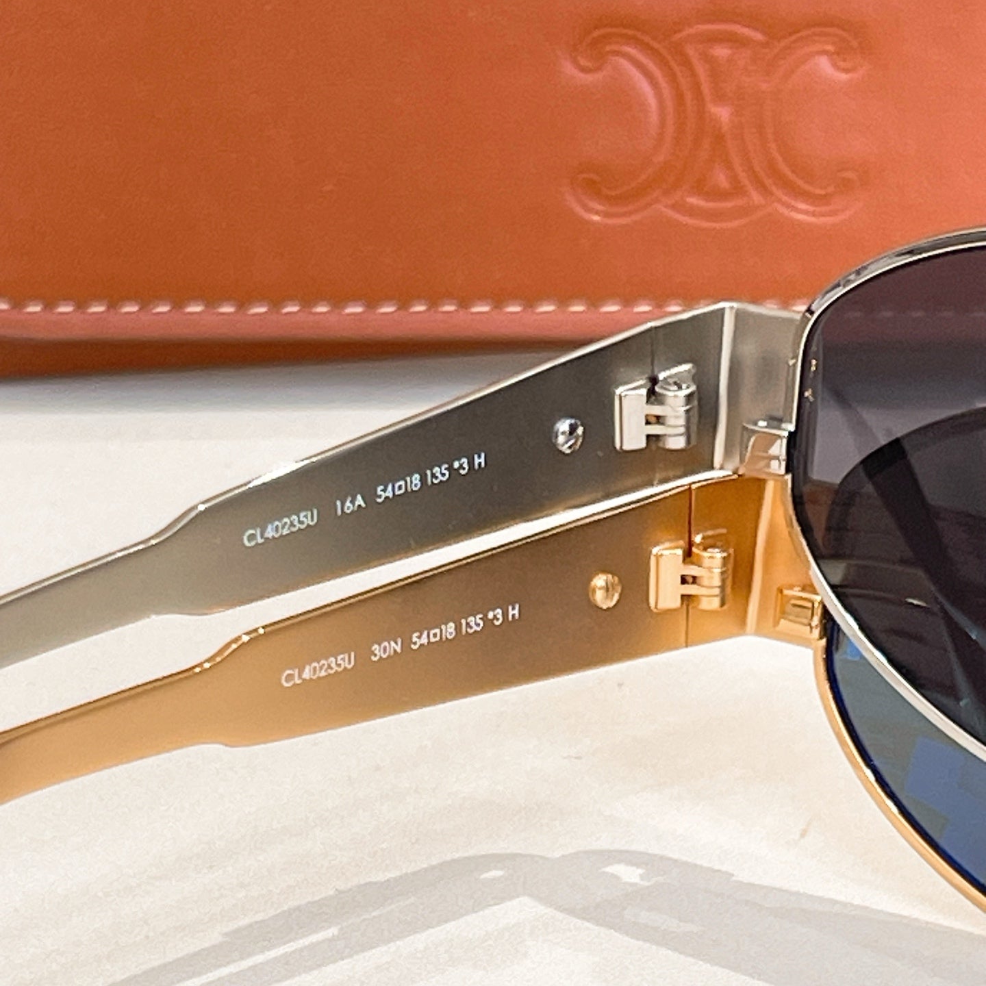 Gold-tone sunglasses side view with dark lenses and metal hinge hardware