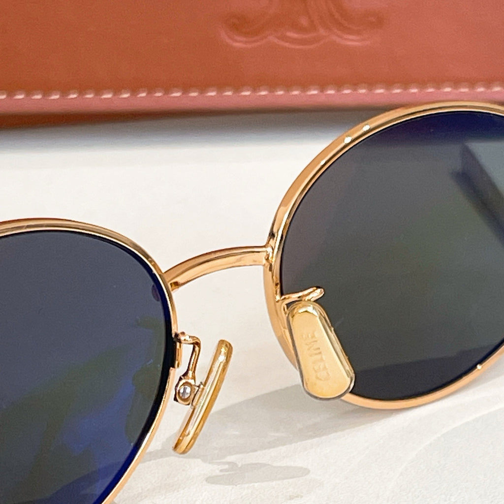 Gold-tone sunglasses close-up with dark lenses and engraved temple hinge
