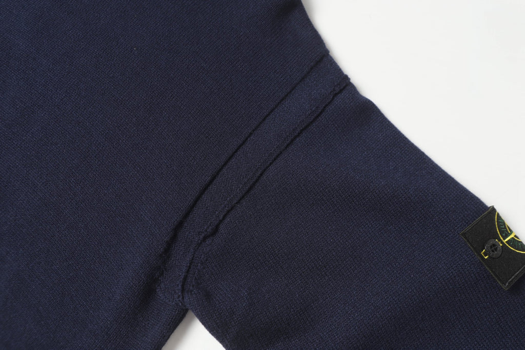 Dark navy knit sweater sleeve with green-gold Stone Island logo patch.