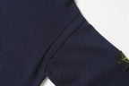 Dark navy knit sweater sleeve with green-gold Stone Island logo patch.