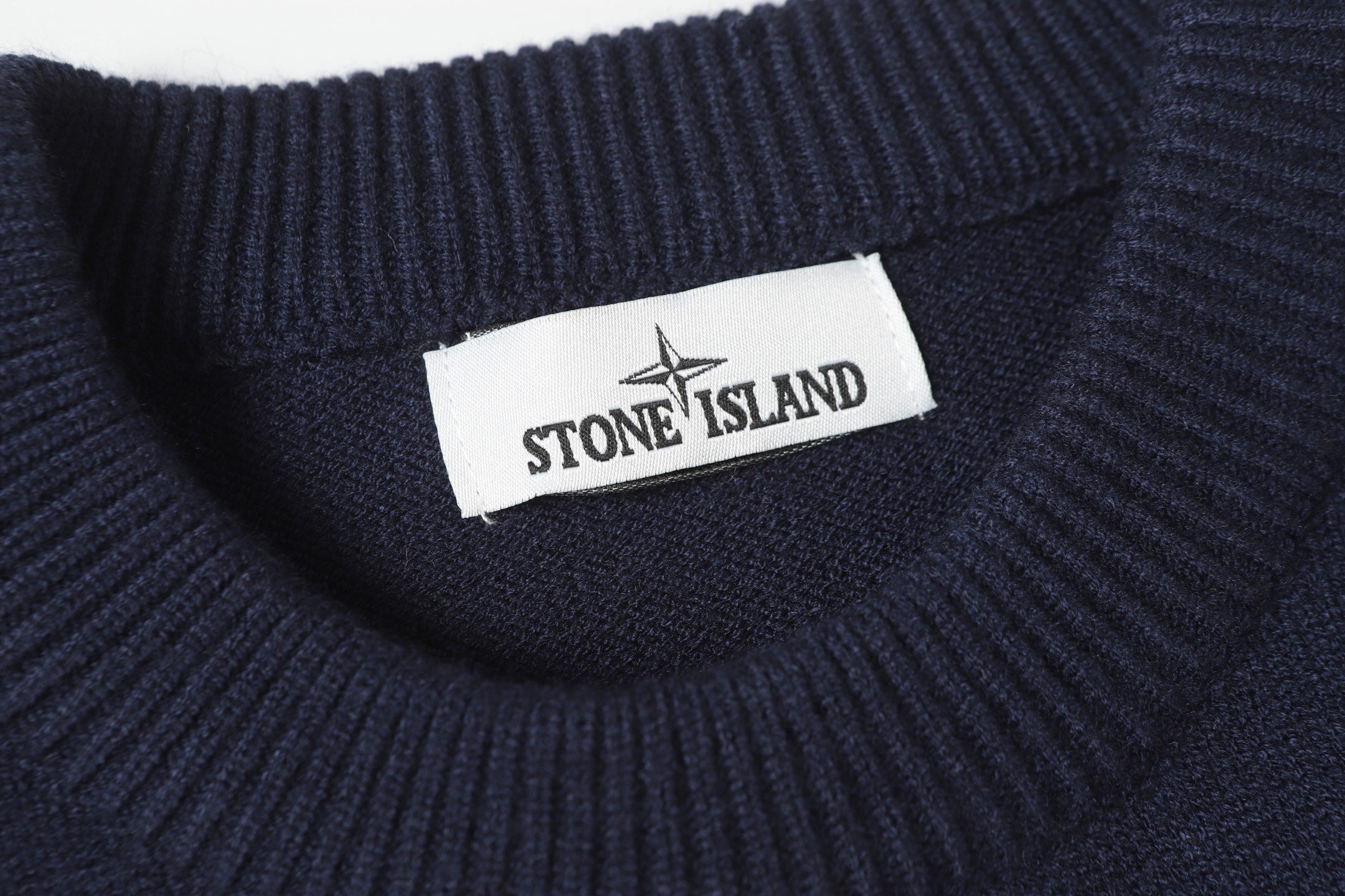 Stone Island logo label at the neck of a dark navy knit sweater.