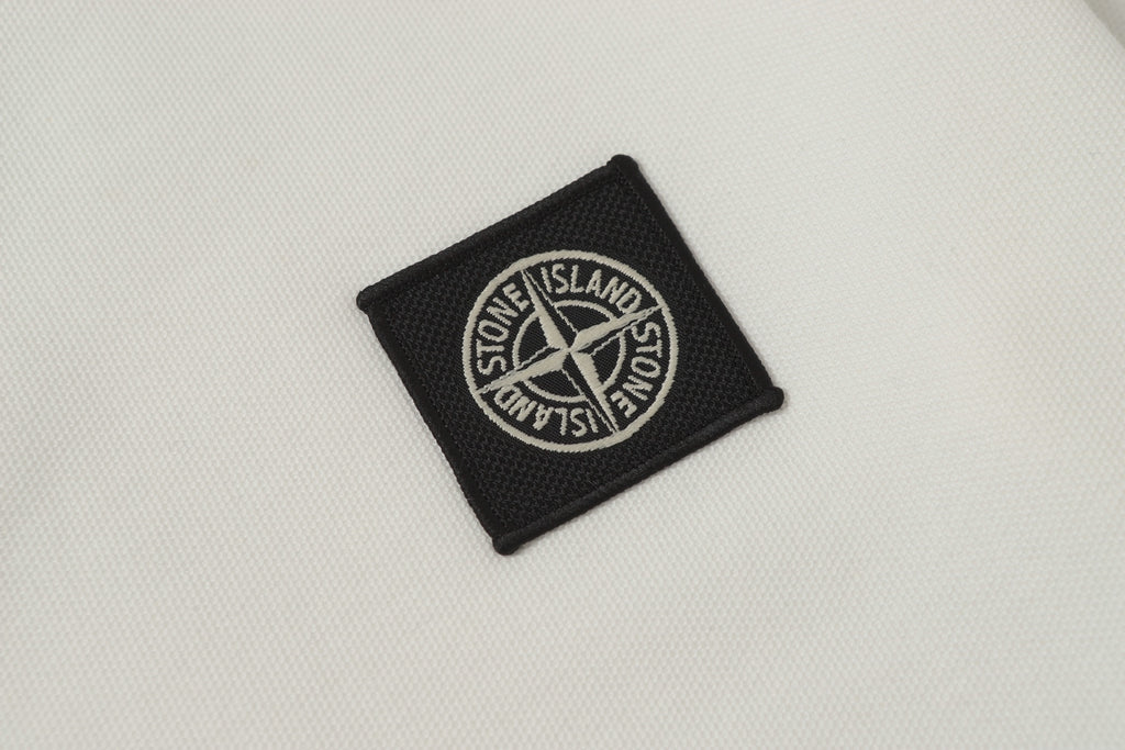 Black Stone Island logo patch on white polo shirt fabric