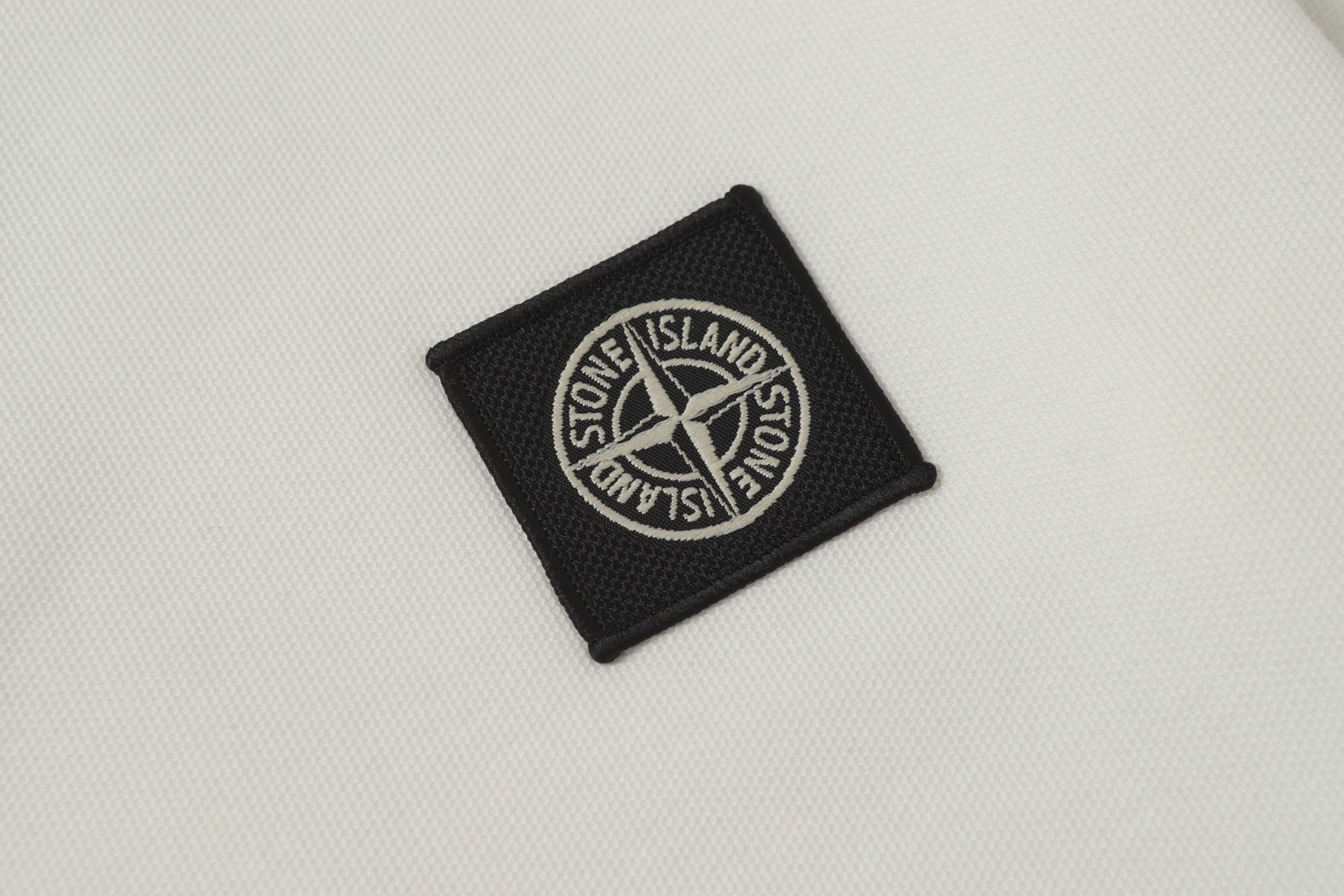 Black Stone Island logo patch on white polo shirt fabric