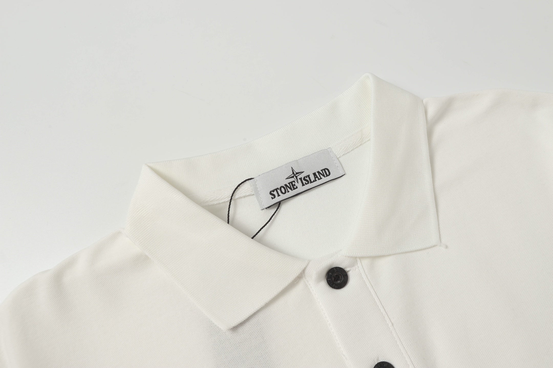 White polo shirt with folded collar and hanging Stone Island label