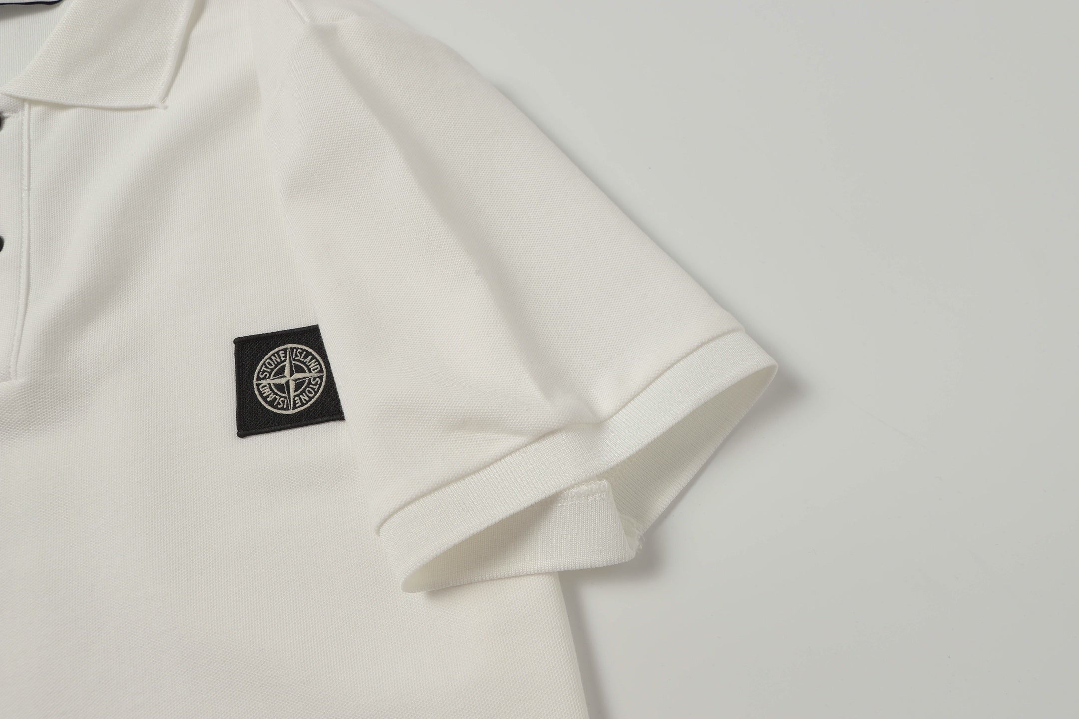 White polo shirt with small black logo patch at left chest