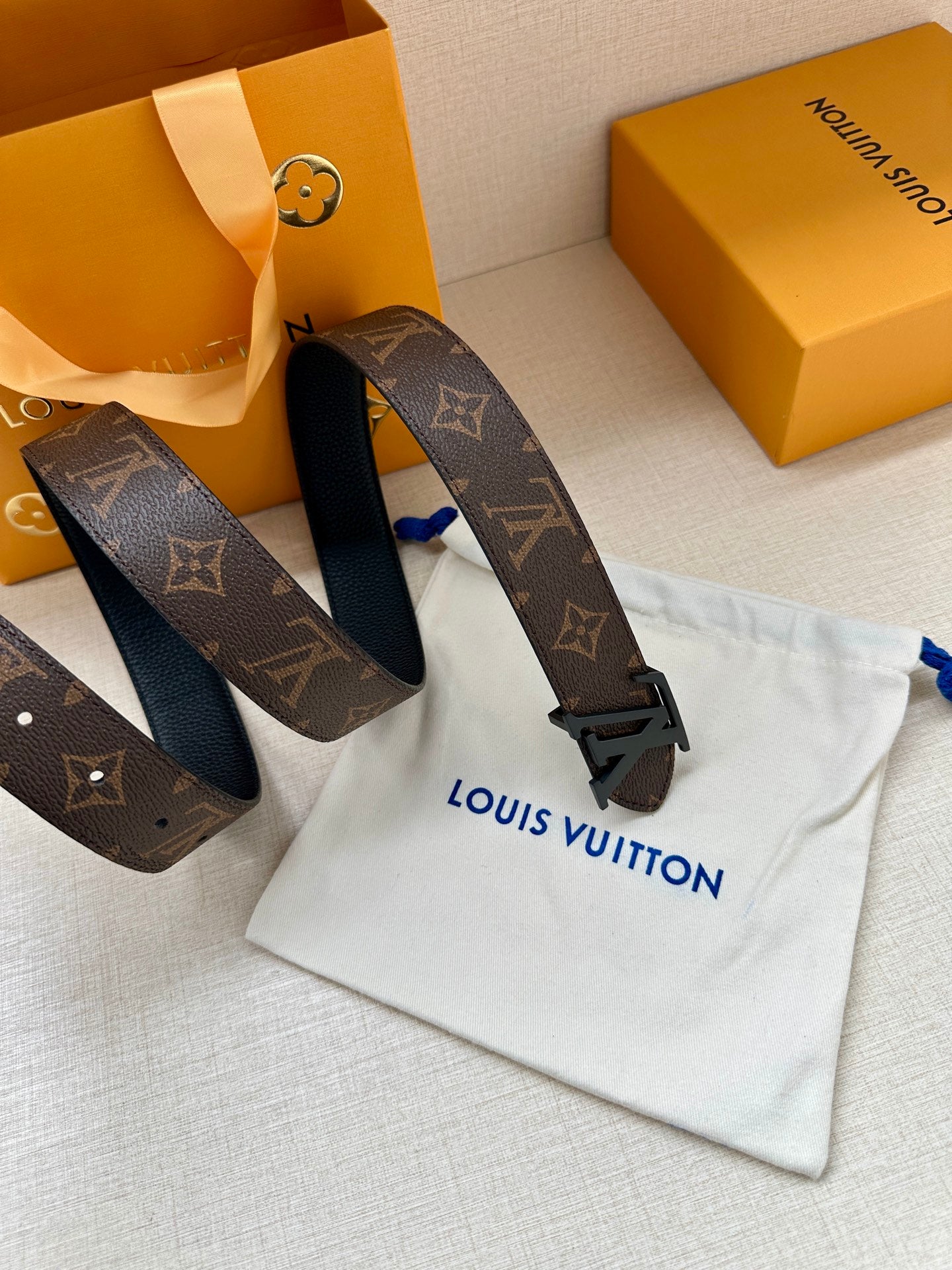 Monogram canvas belt with dark strap loops and black LV buckle, laid on cloth