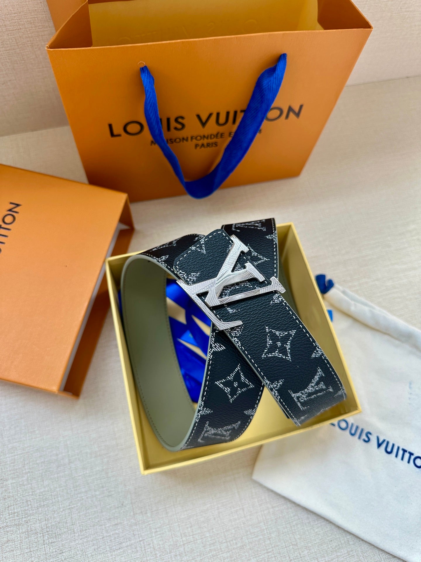 Louis Vuitton monogram belt laid flat with silver-tone buckle on dust bag