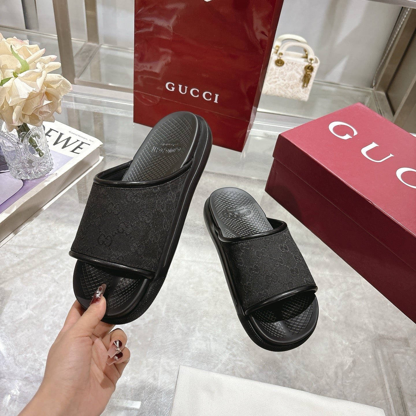 Gucci black slide sandals with monogram strap; shopper holds one sandal by heel